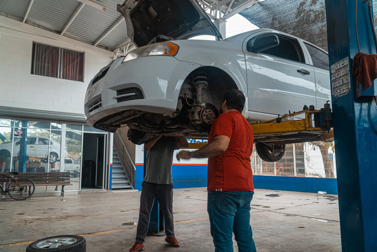 Two technicians inspecting a car raised on a lift in a repair bay