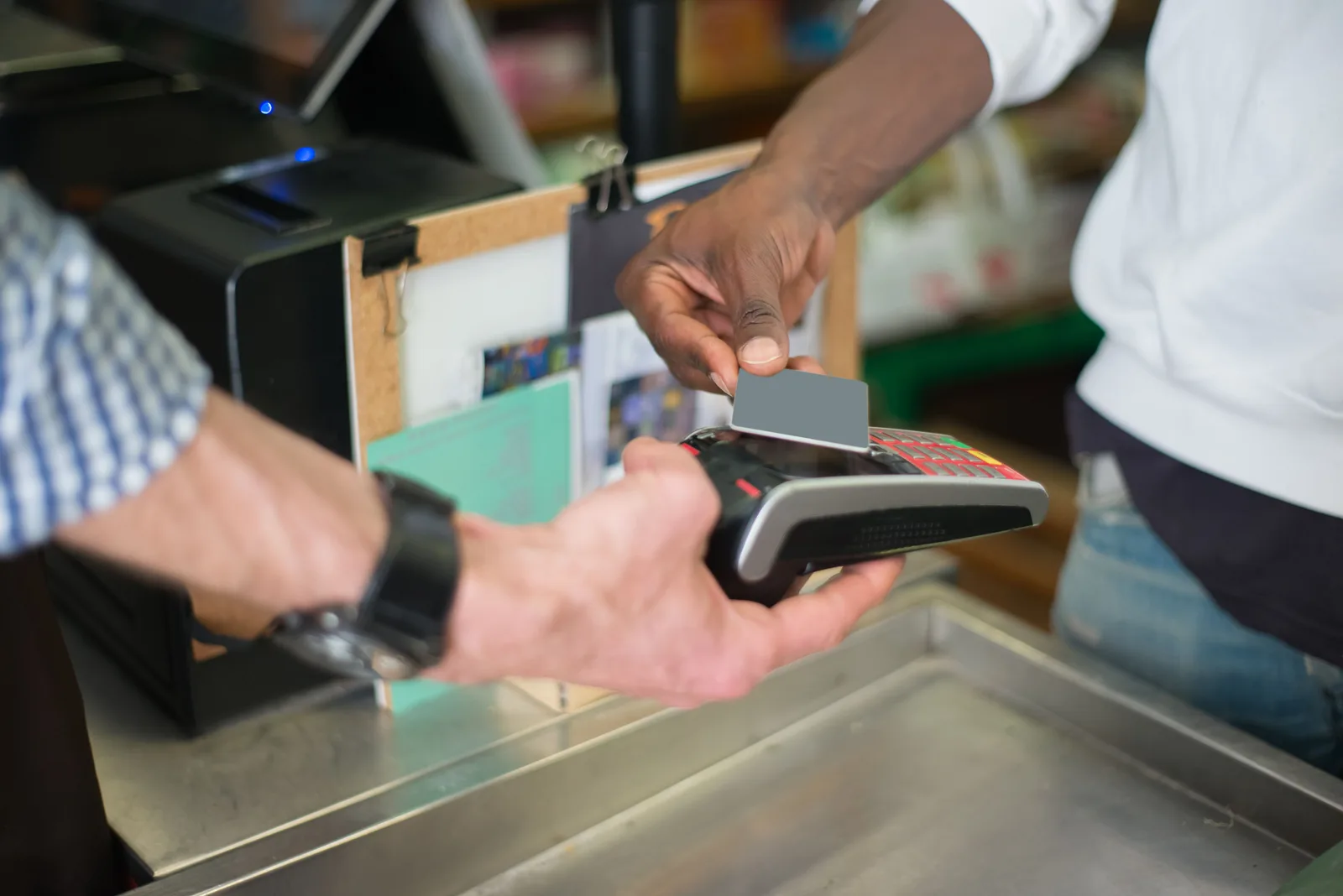 A customer tapping a bank card on a card reader held out by a shop assistant at a checkout counter