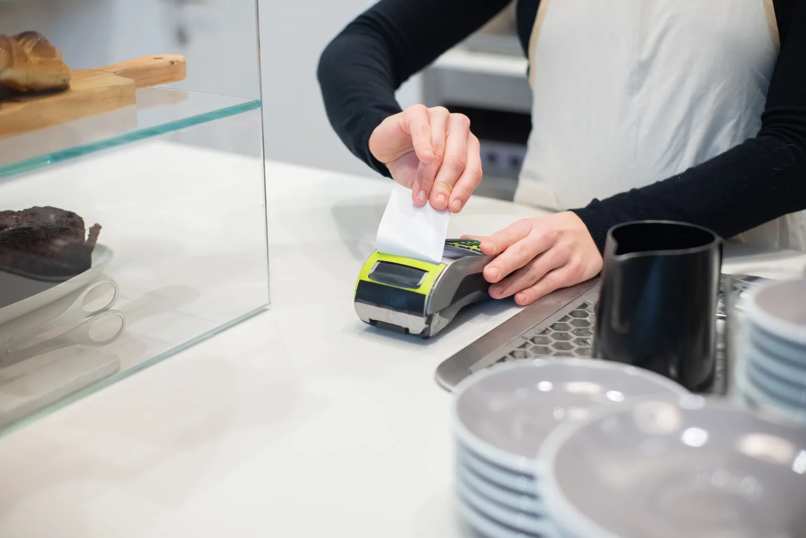 A receipt printing from a card terminal on a cafe counter beside a pastry case