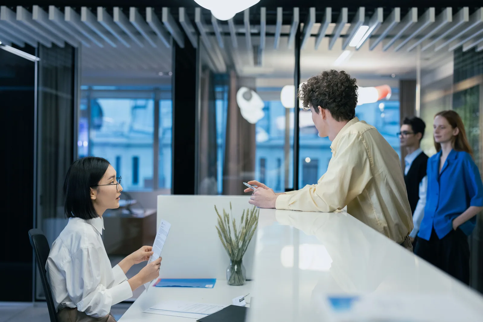 Colleagues talking across a white desk in a glass fronted office