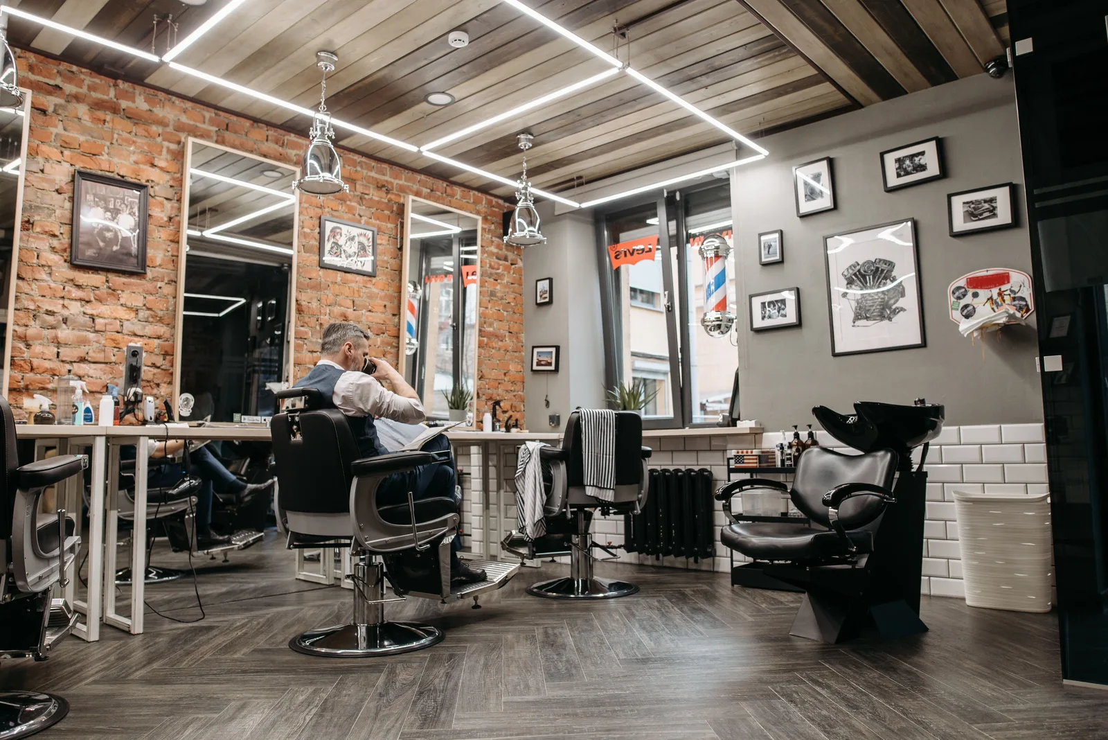 Barbershop floor with several styling chairs and wall mirrors, one barber working on a client at the far station