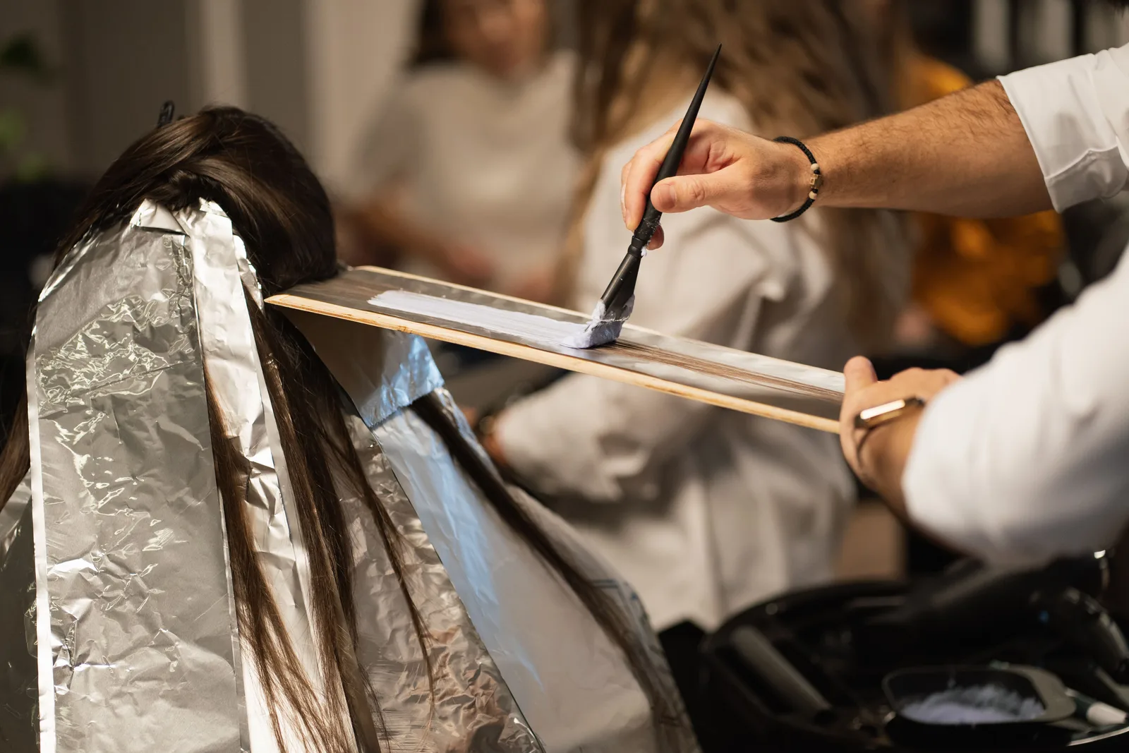 A stylist brushing colour onto a section of hair held on a foil during a highlighting service in a salon.
