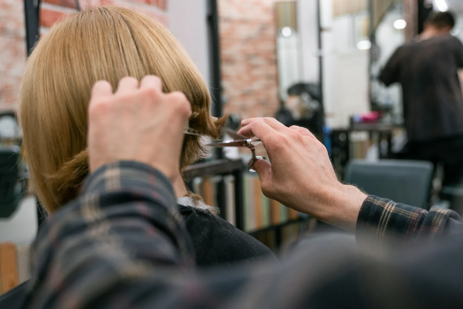 A stylist cutting the hair of a seated client at a salon station, with other chairs in use behind them.