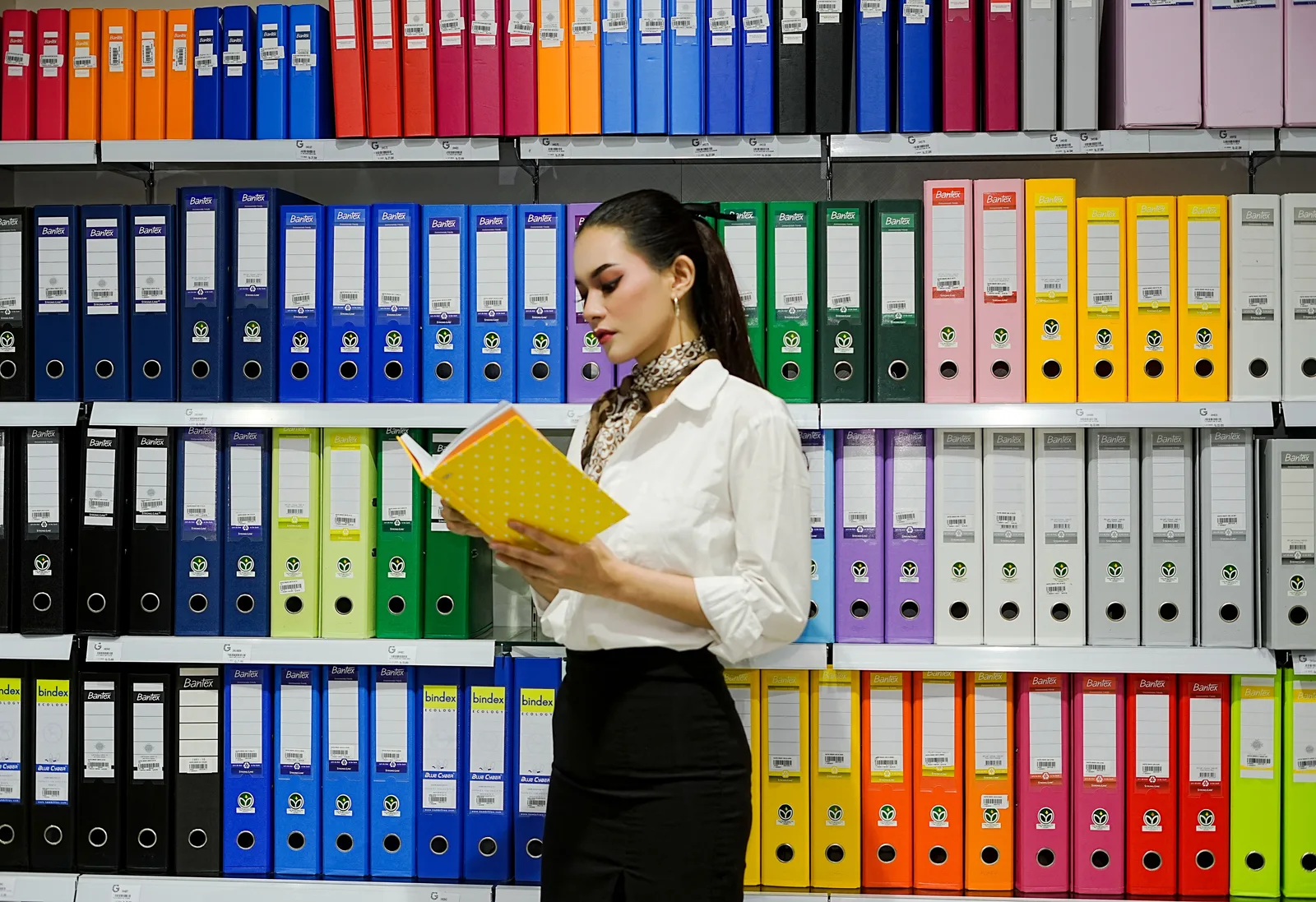 Person reading a file in front of shelves of color coded lever arch binders