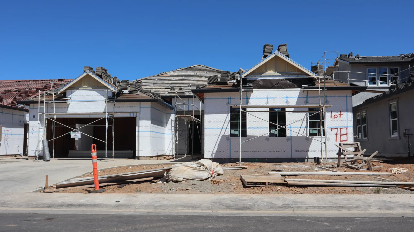 A single family house under construction with scaffolding, exposed sheathing and roof tiles stacked on the roof