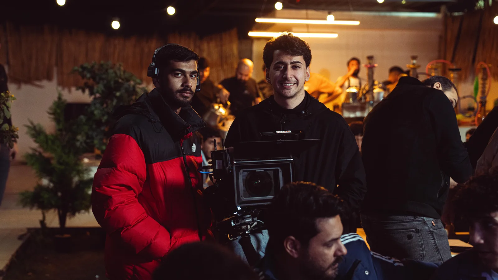 A camera operator wearing headphones and two crew members working around a cinema camera on an indoor film set.
