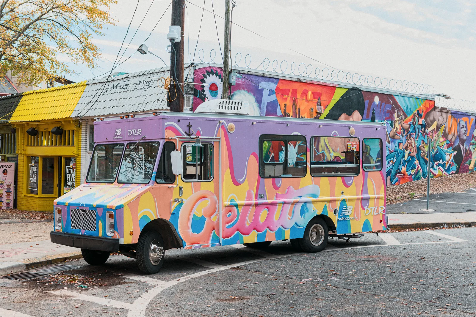Un camión de gelato pintado de colores brillantes estacionado junto a un gran mural callejero en una esquina