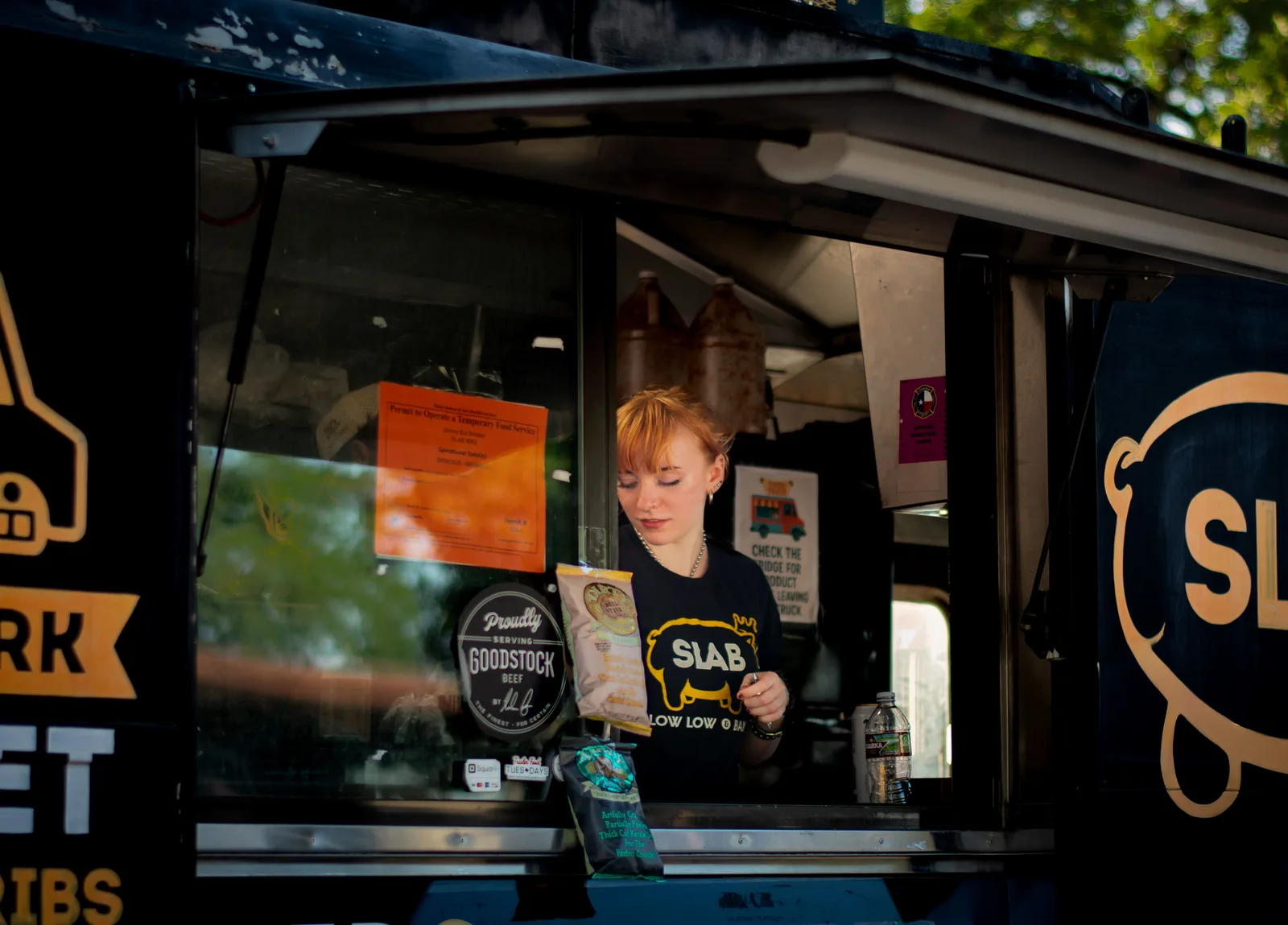 A worker bagging an order inside the service window of a barbecue food trailer at night in Austin, Texas