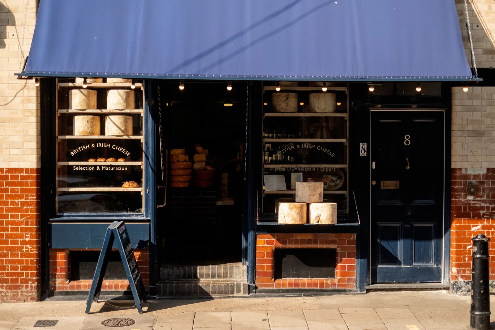 Independent specialist food shop with cheese stacked in the window under a fabric awning