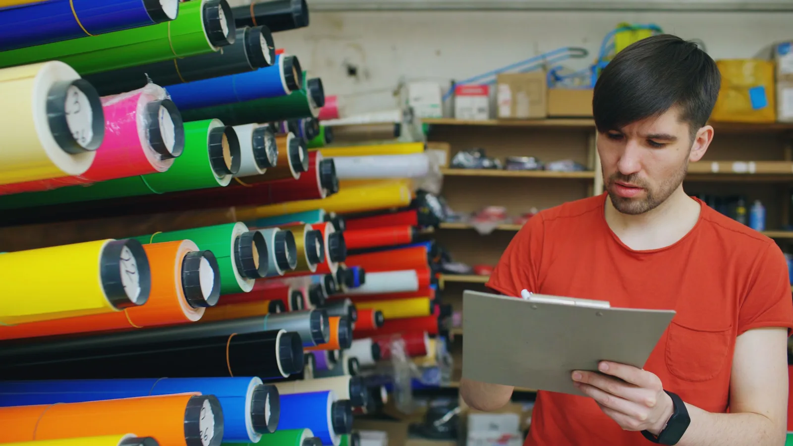 Shopkeeper working through a stock list on a tablet in front of racked rolls of material.