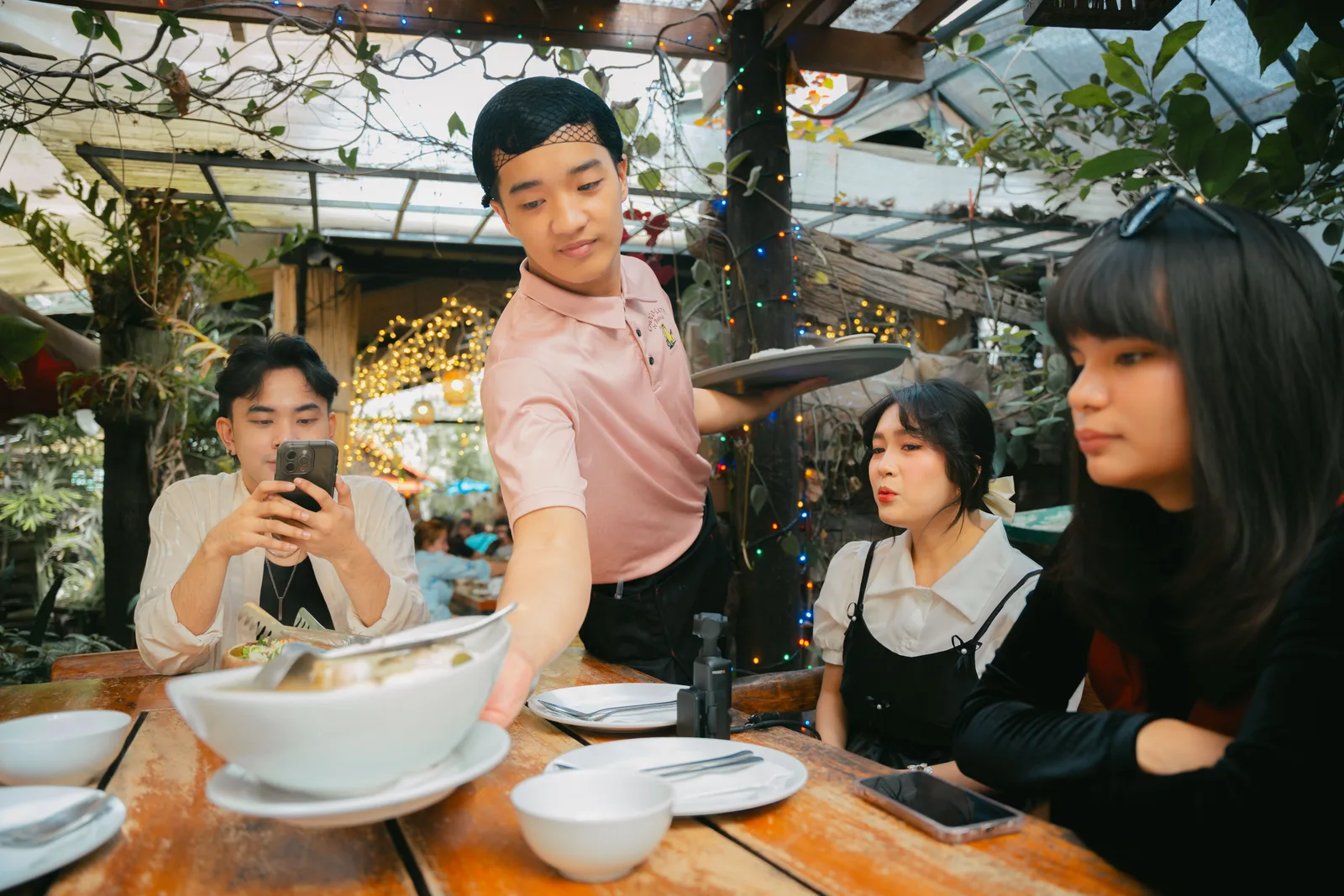 Waiter setting dishes down at an outdoor restaurant table strung with lights