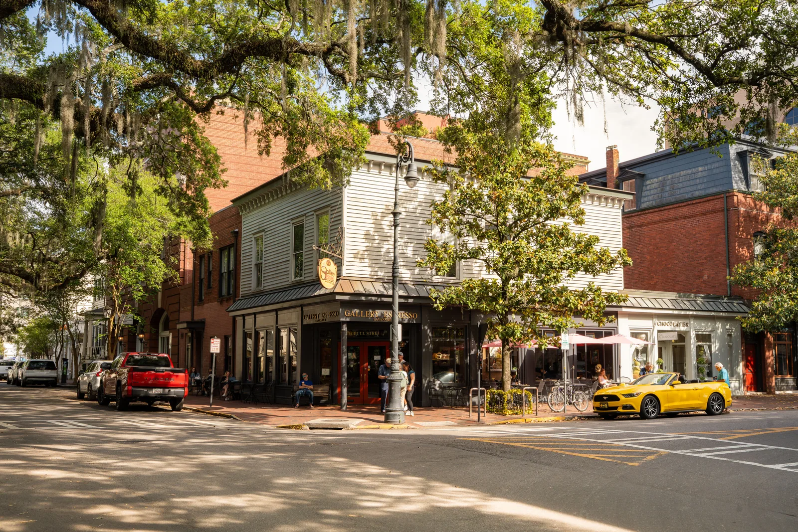 A corner shop building under live oaks draped in Spanish moss on a downtown Savannah street, with cars parked along the kerb