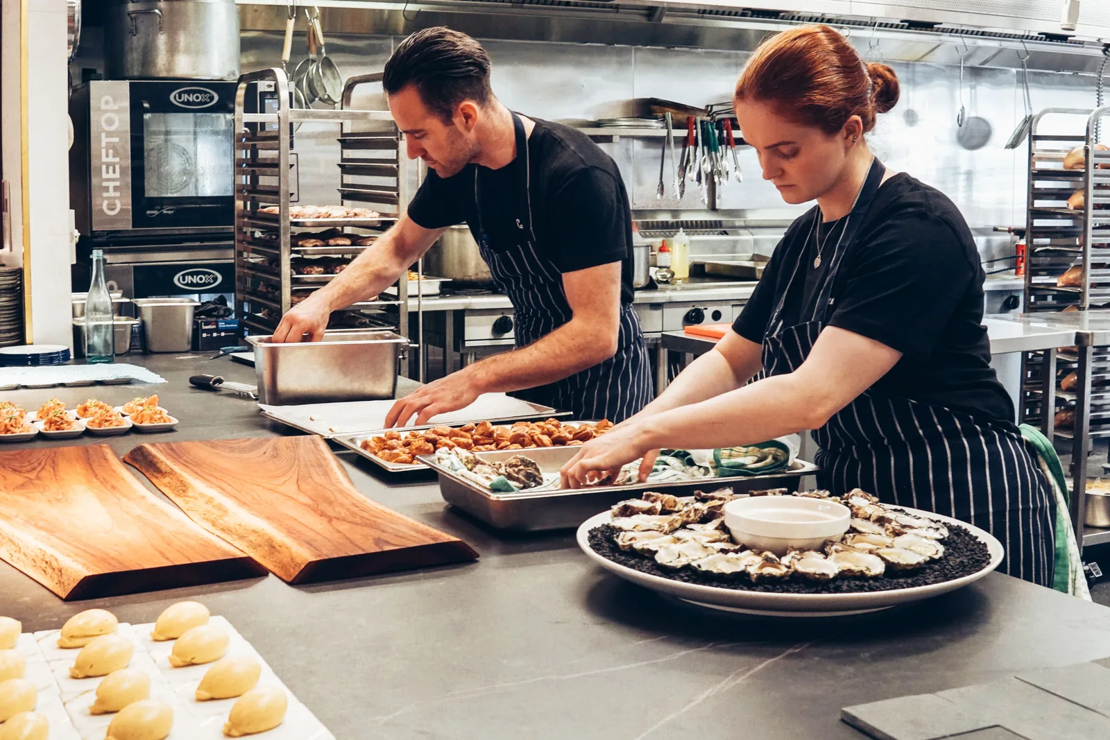 Dos cocineros sirviendo platos uno junto al otro en la línea de una cocina de restaurante concurrida.