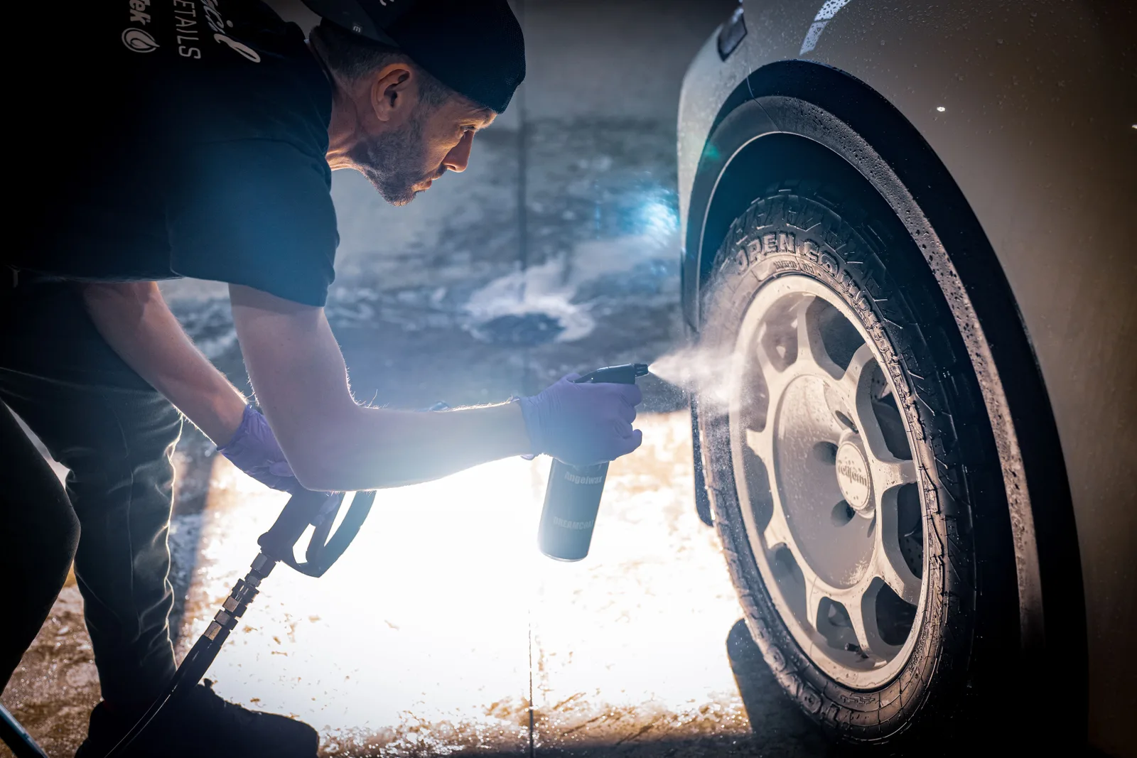 A man cleaning a car tire with a spray bottle in a vehicle detailing shop