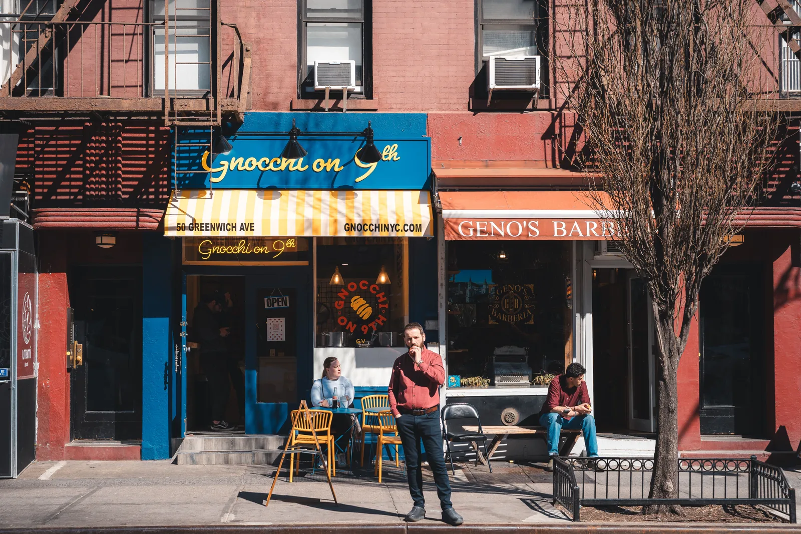 A small restaurant and a barbershop side by side on a Greenwich Village street in New York City, with customers seated at tables on the sidewalk.