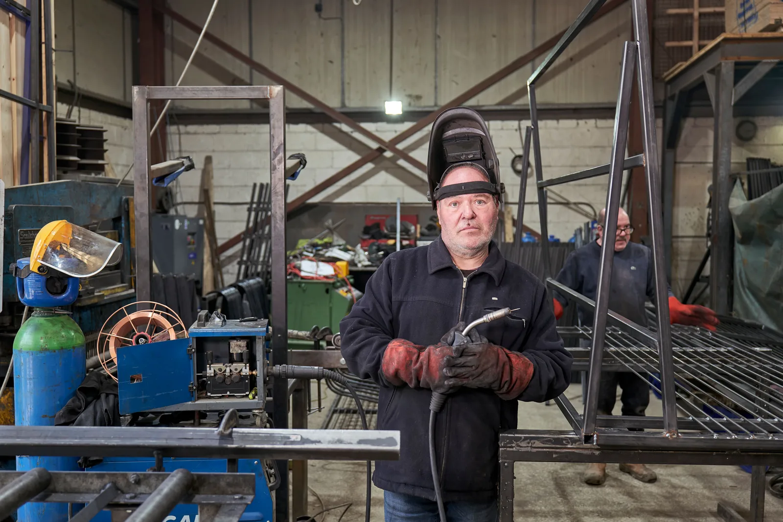 Two welders working steel sections on the floor of a fabrication shop