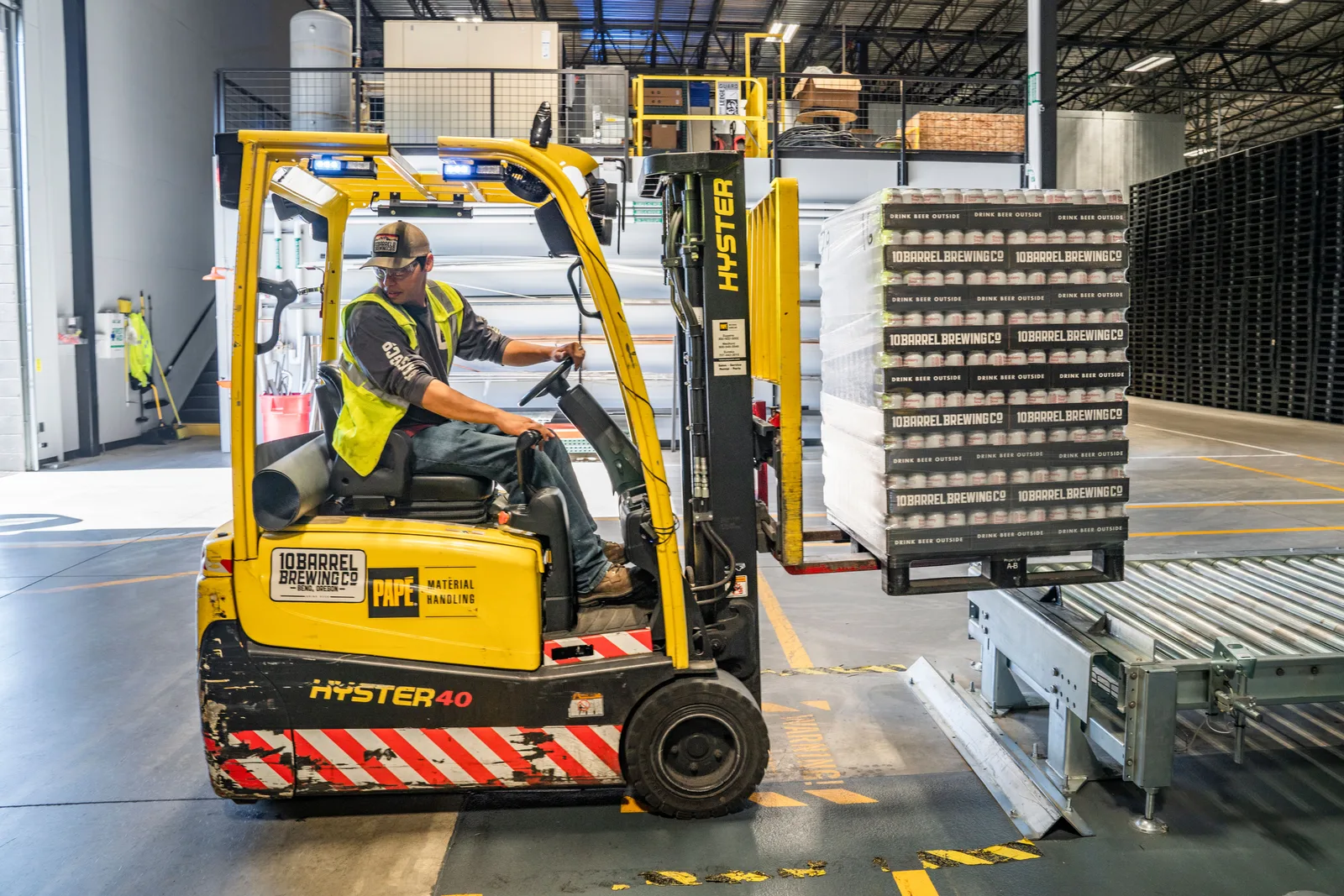 A forklift operator moving stacked wooden crates through a warehouse.