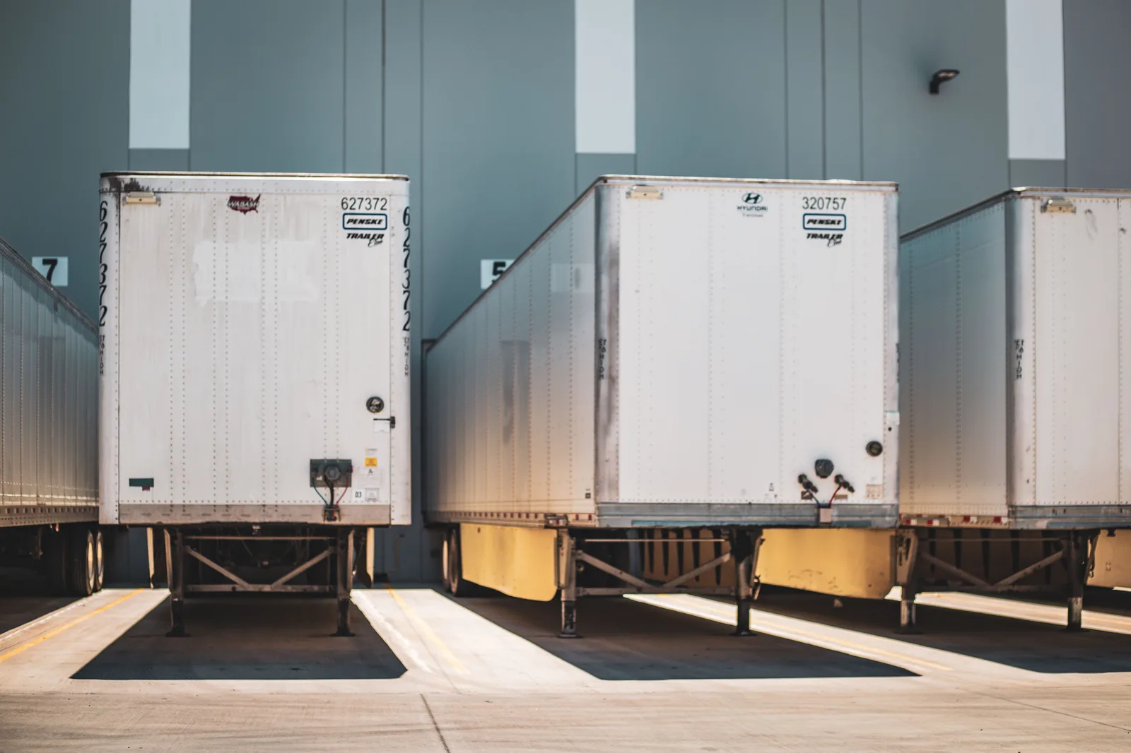 Three freight trailers backed into numbered dock doors at a warehouse.