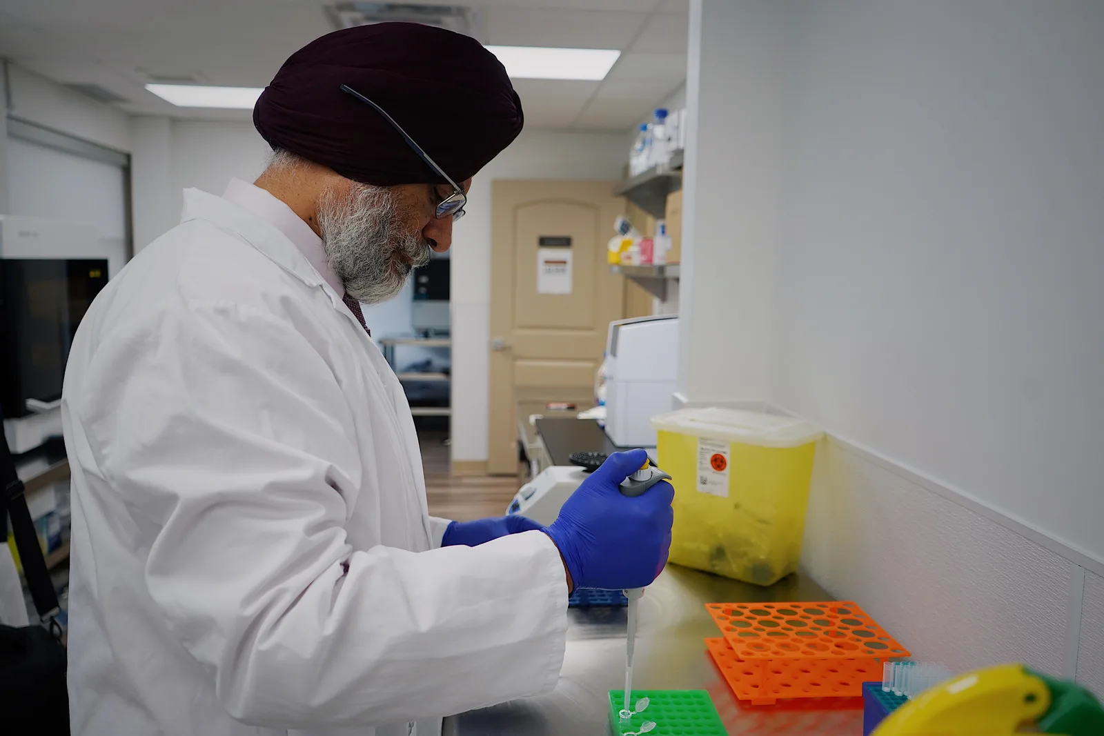 A laboratory technician in a white coat using a pipette to fill a sample tray on a bench.