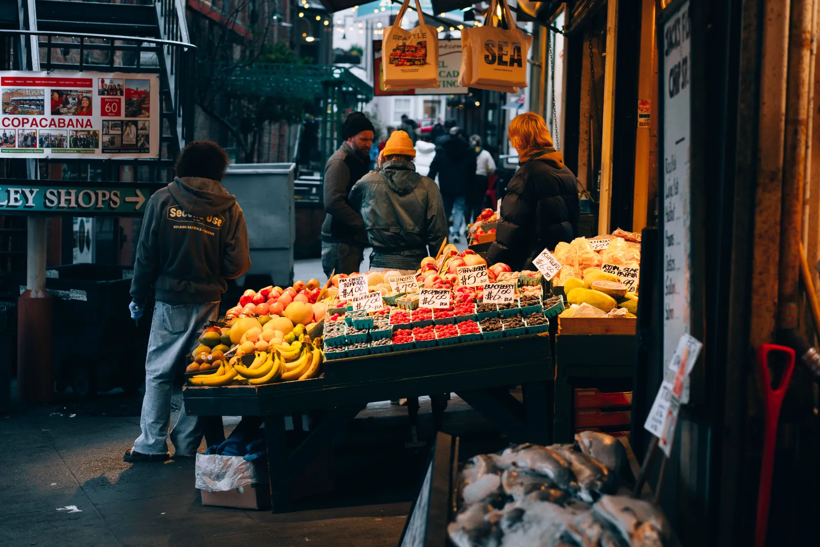 Fruit and produce laid out on market stalls in Seattle, with vendors and shoppers at the counter