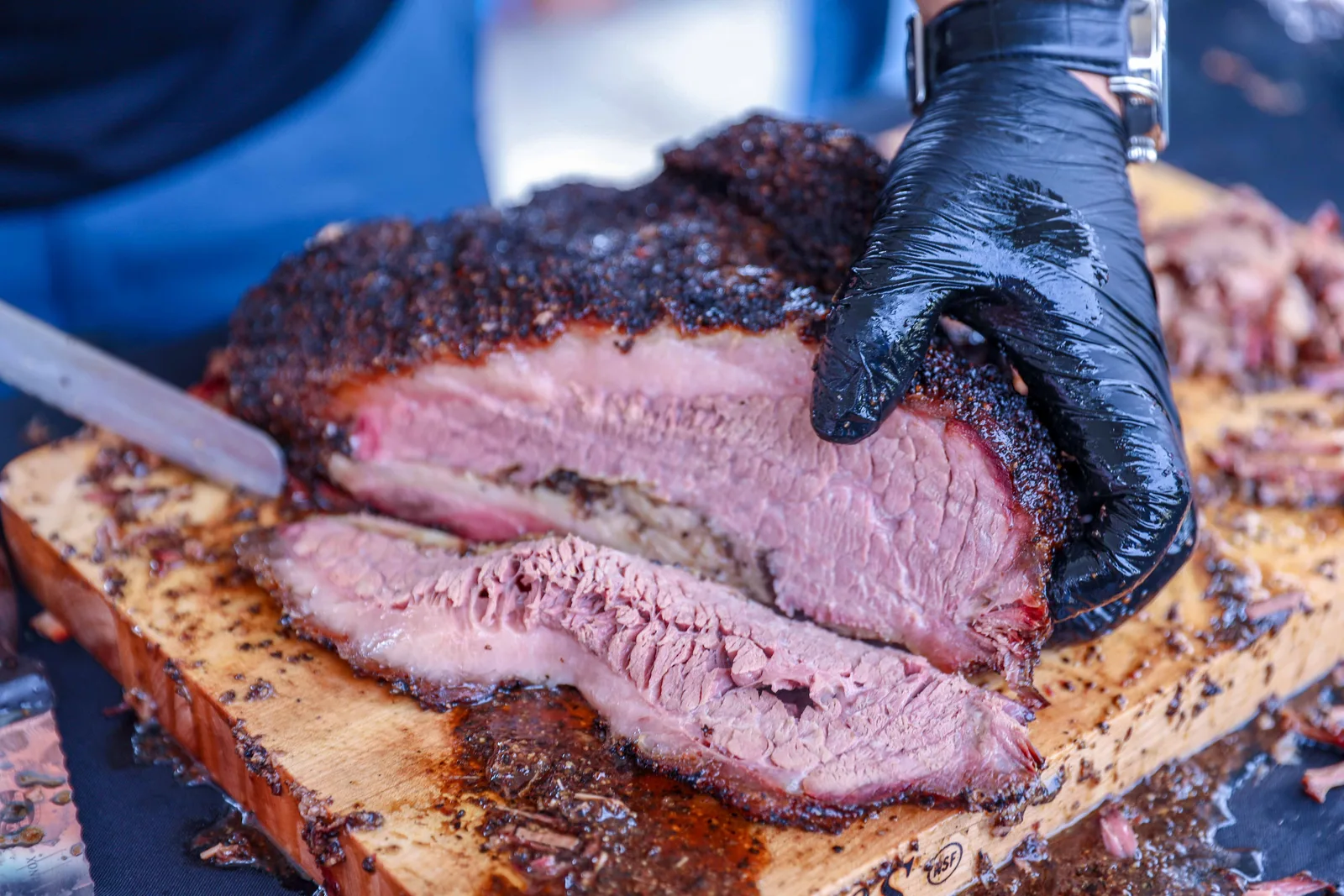 Gloved hands slicing a smoked beef brisket on a wooden board