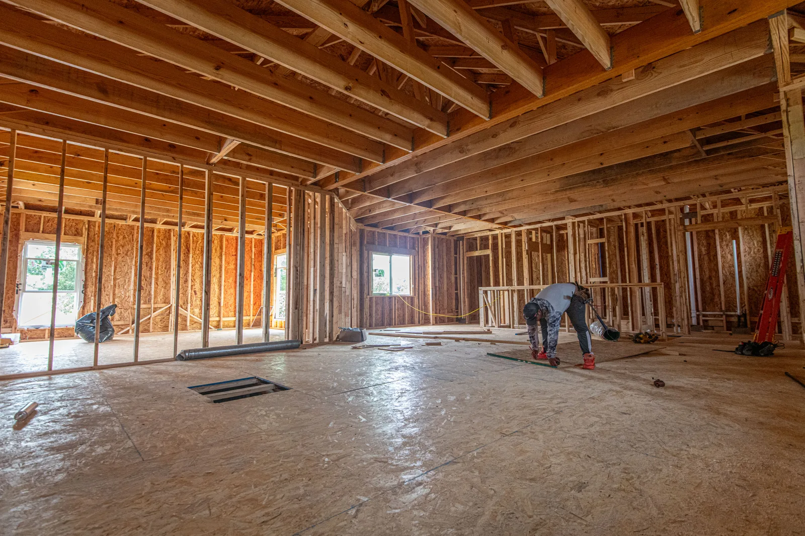 Interior de una casa de estructura de madera en construcción, con un trabajador al fondo.