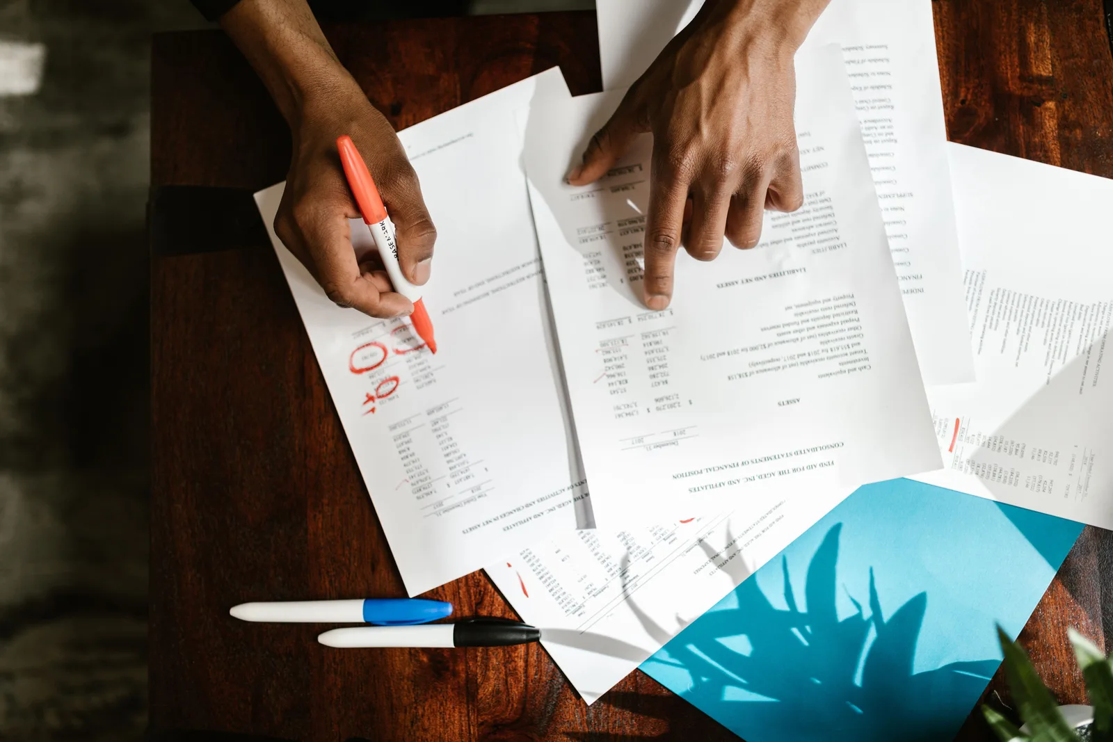 Overhead view of a person marking up printed financial statements with a highlighter on a desk.