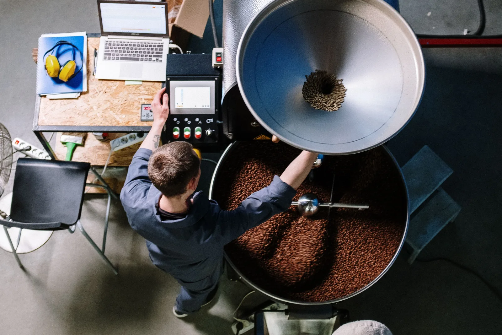 Worker standing over a drum roaster full of beans in a coffee roastery