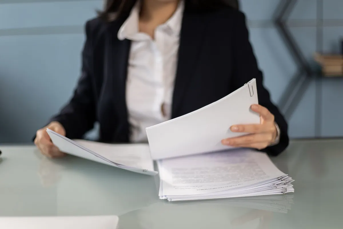 Businesswoman in a dark blazer reviewing and organizing papers at an office desk.