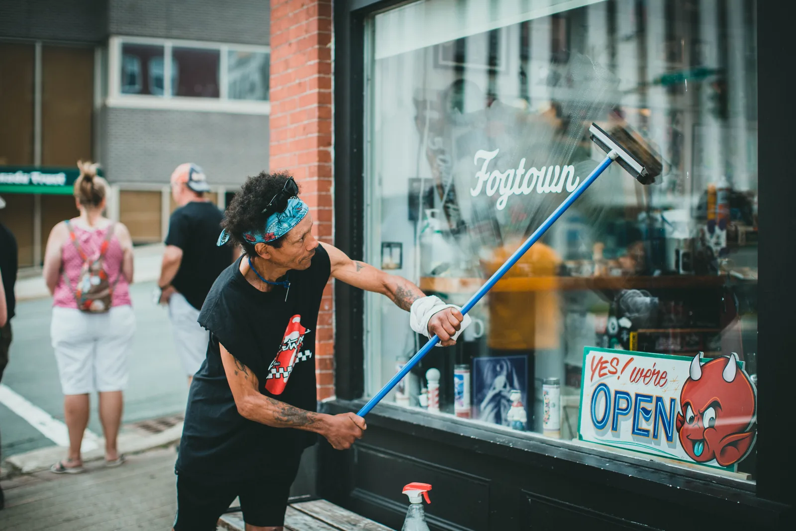 A worker squeegeeing the glass of a storefront window from the pavement.