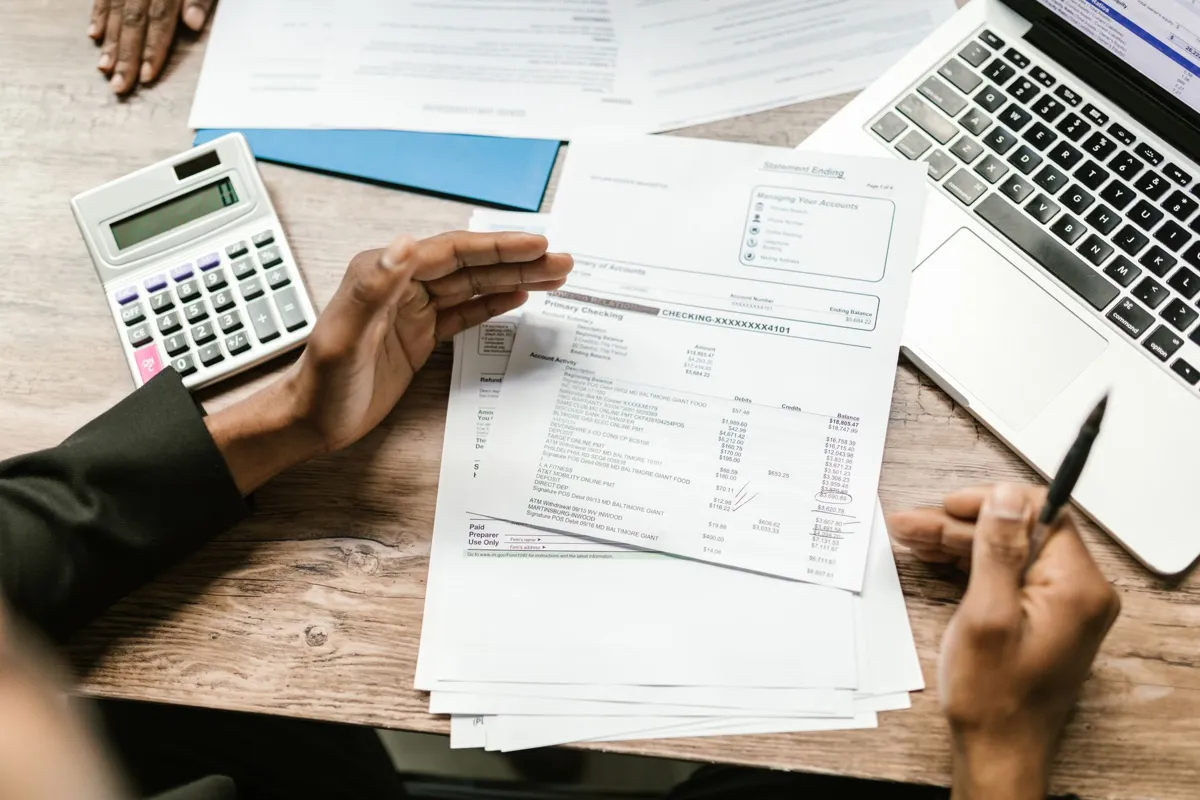Business owner at a desk with printed account statements, a calculator and a laptop, going through offer paperwork line by line