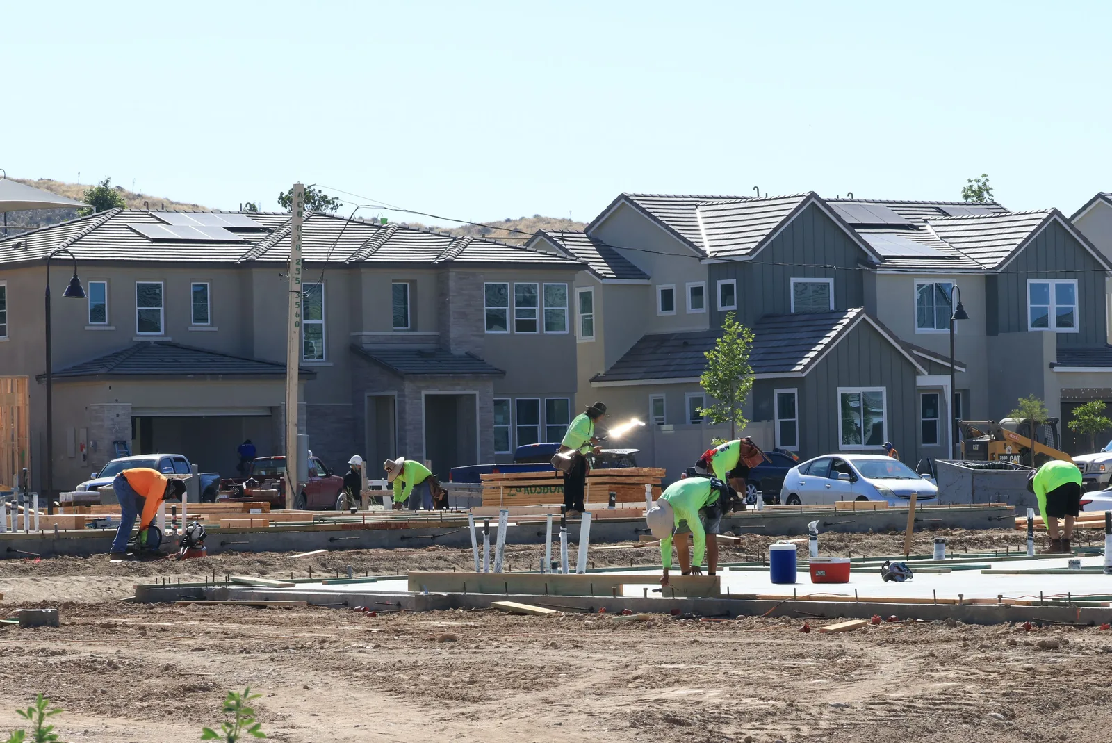 A crew working on concrete foundations across a residential development, with framed and finished houses behind them.