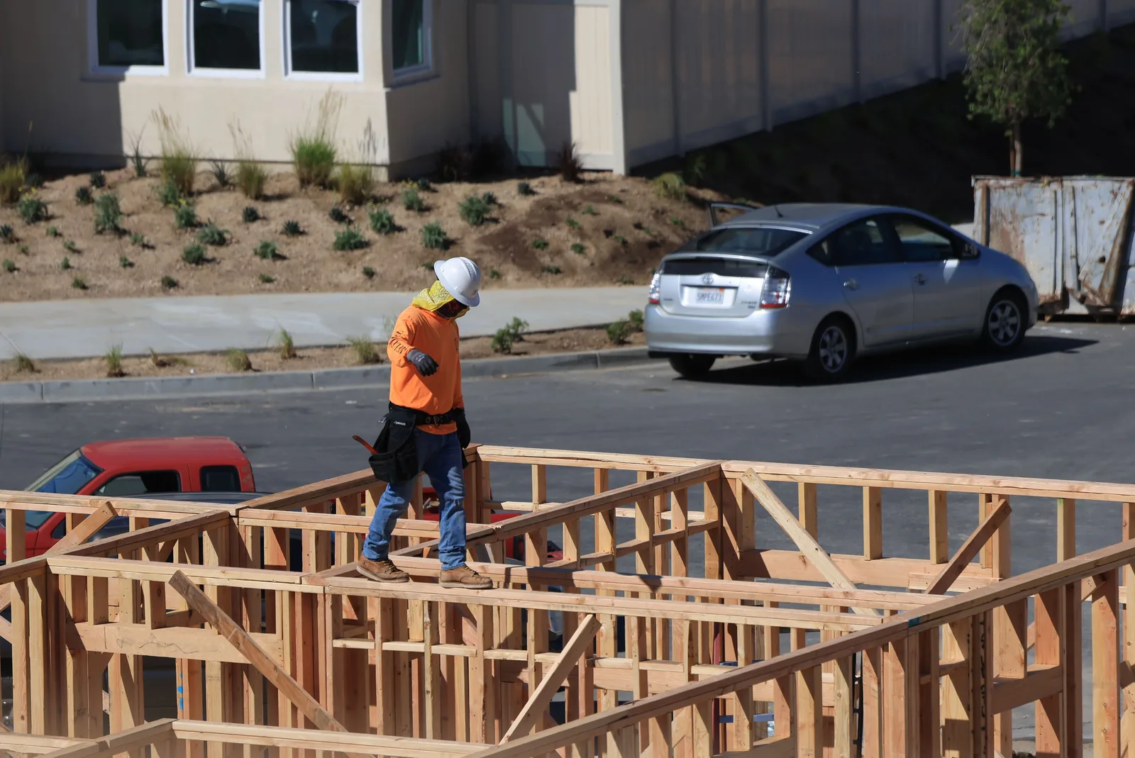 A construction worker in a hard hat and high visibility vest walking across the timber floor framing of a house under construction.