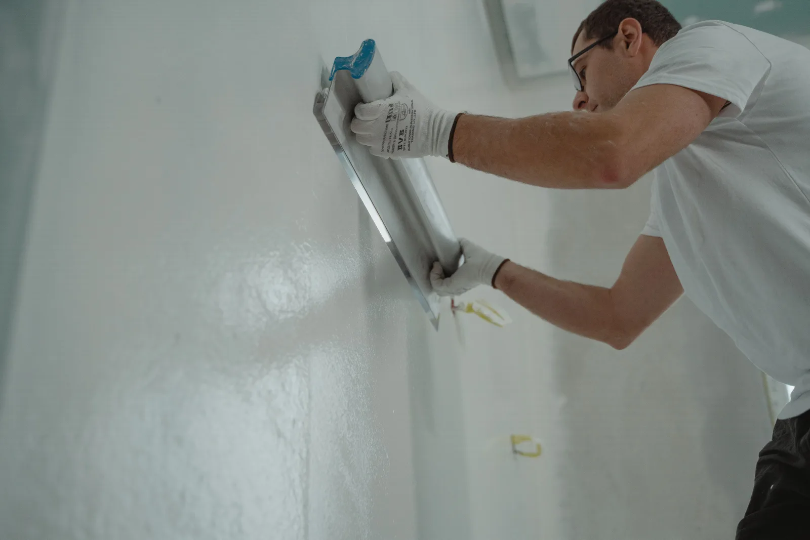 Worker in gloves skimming a wall smooth with a wide plastering trowel
