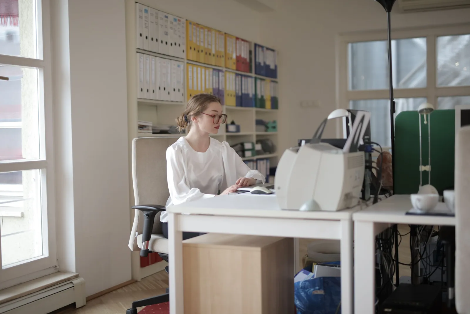 An accountant working at a desk in an office lined with shelves of labelled box files.