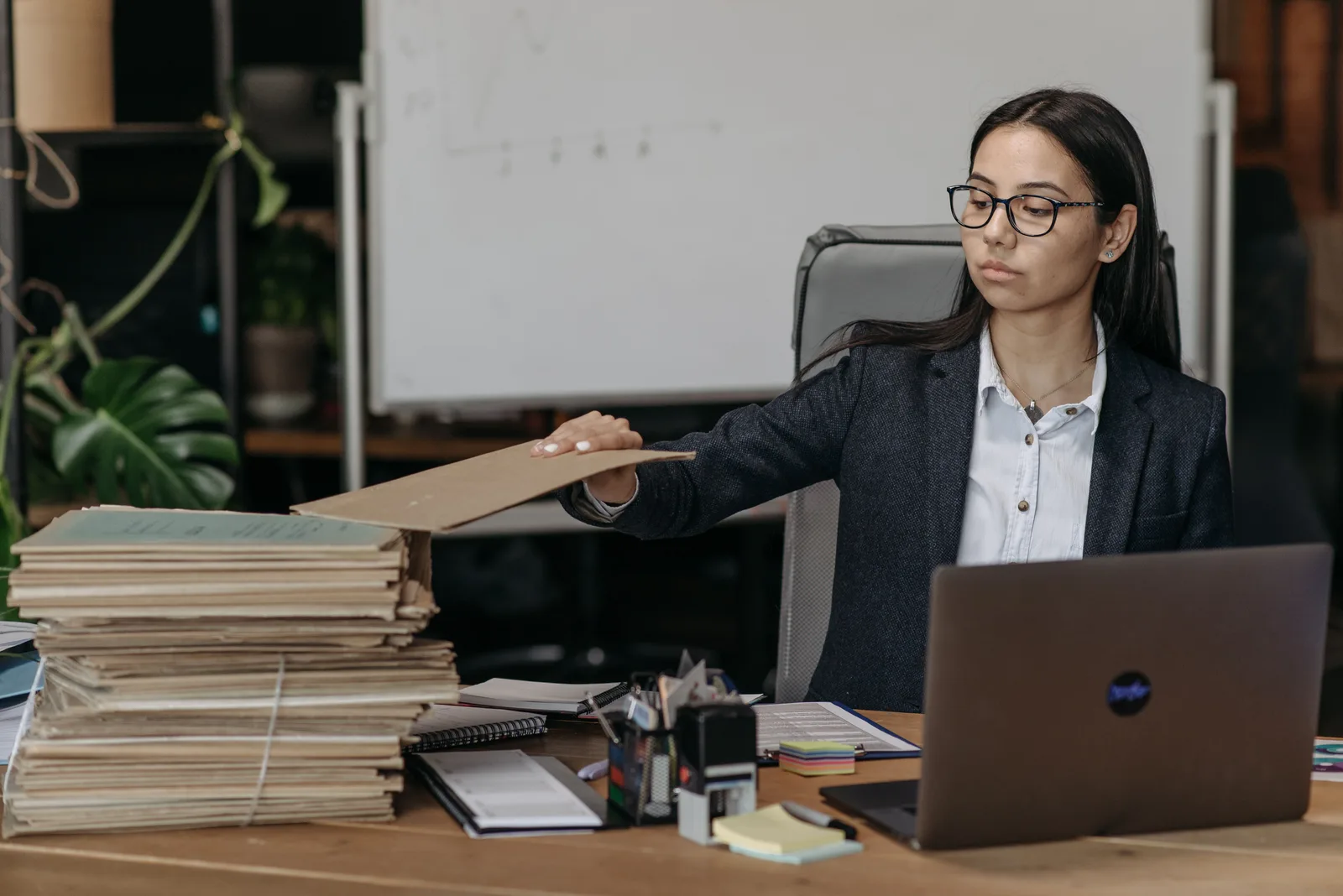 A bookkeeper opening a folder at a desk stacked with bundled client ledgers and papers.