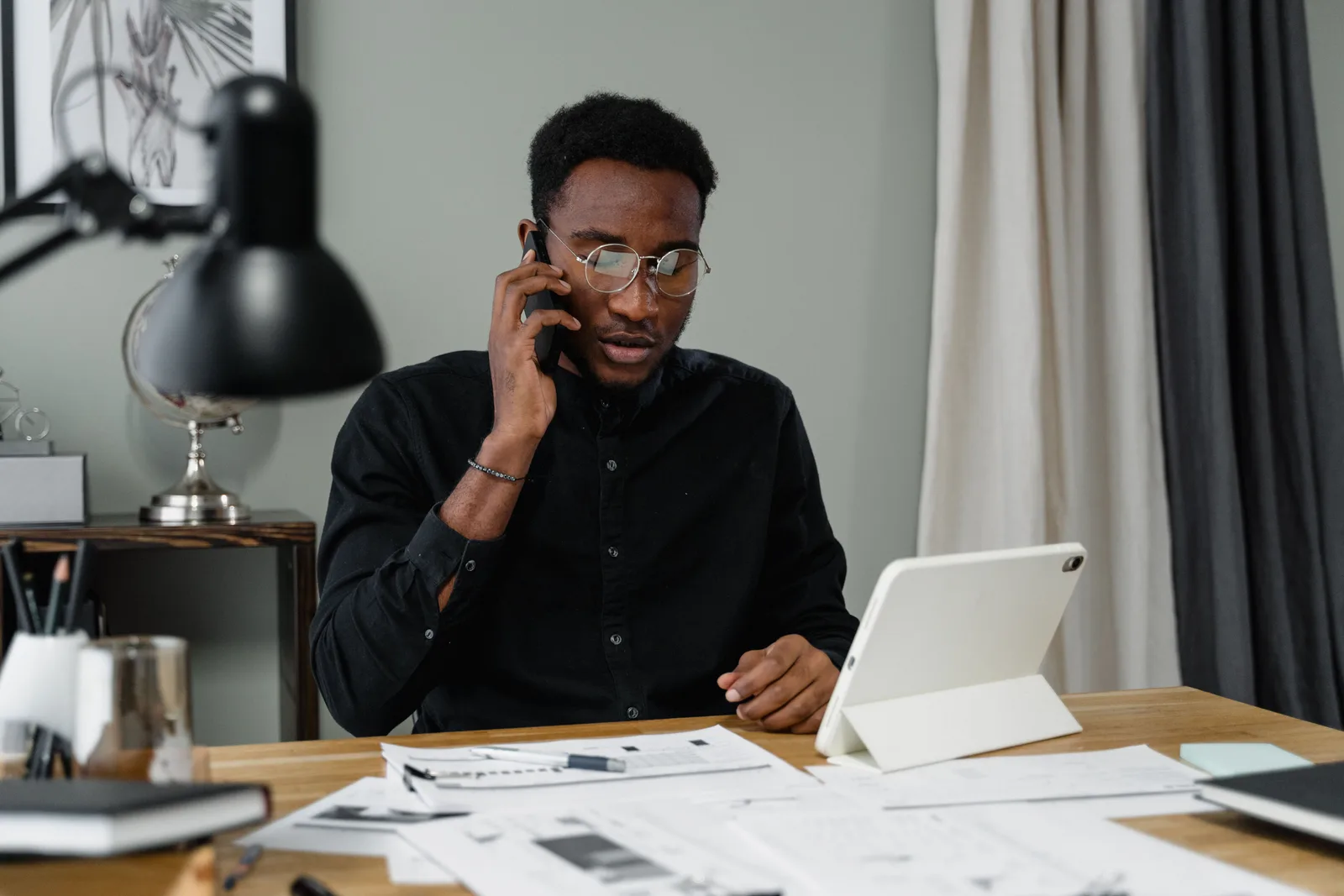 Man taking a phone call at a desk with a tablet and printed documents in front of him