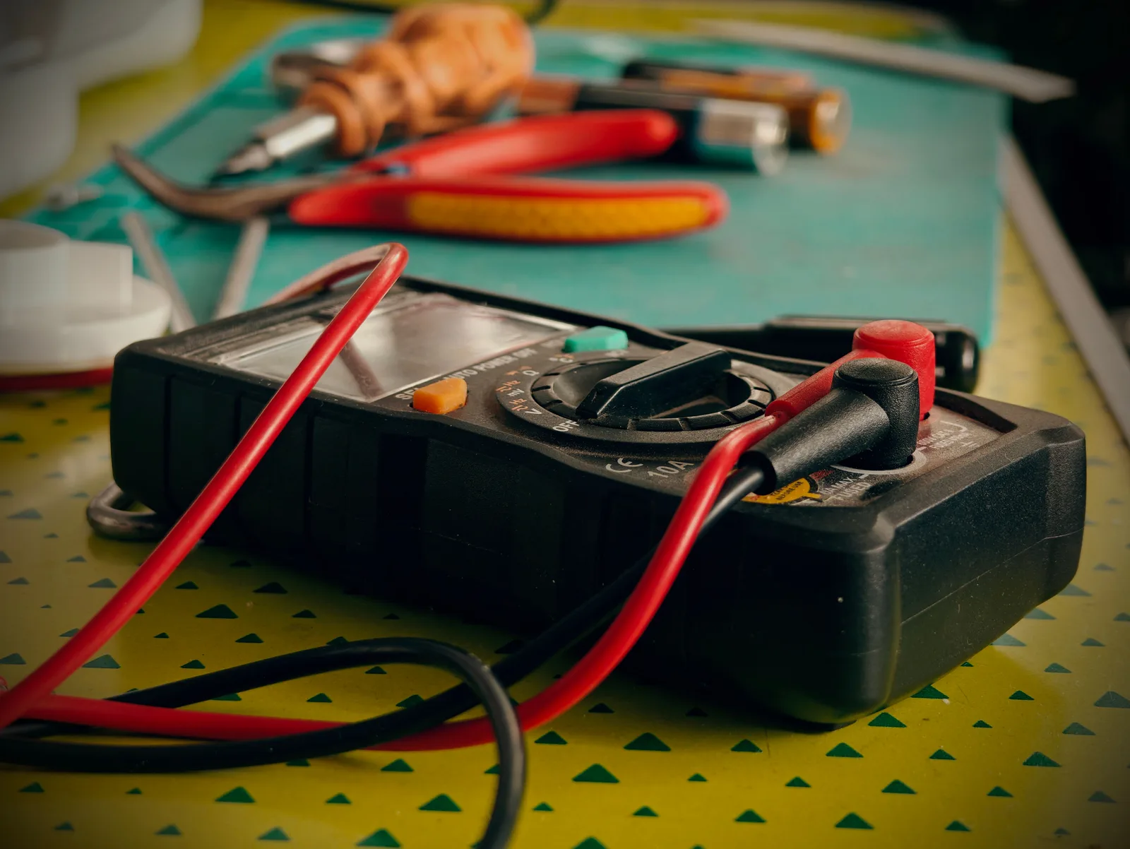 Multimeter with test leads and hand tools laid out on a work bench.