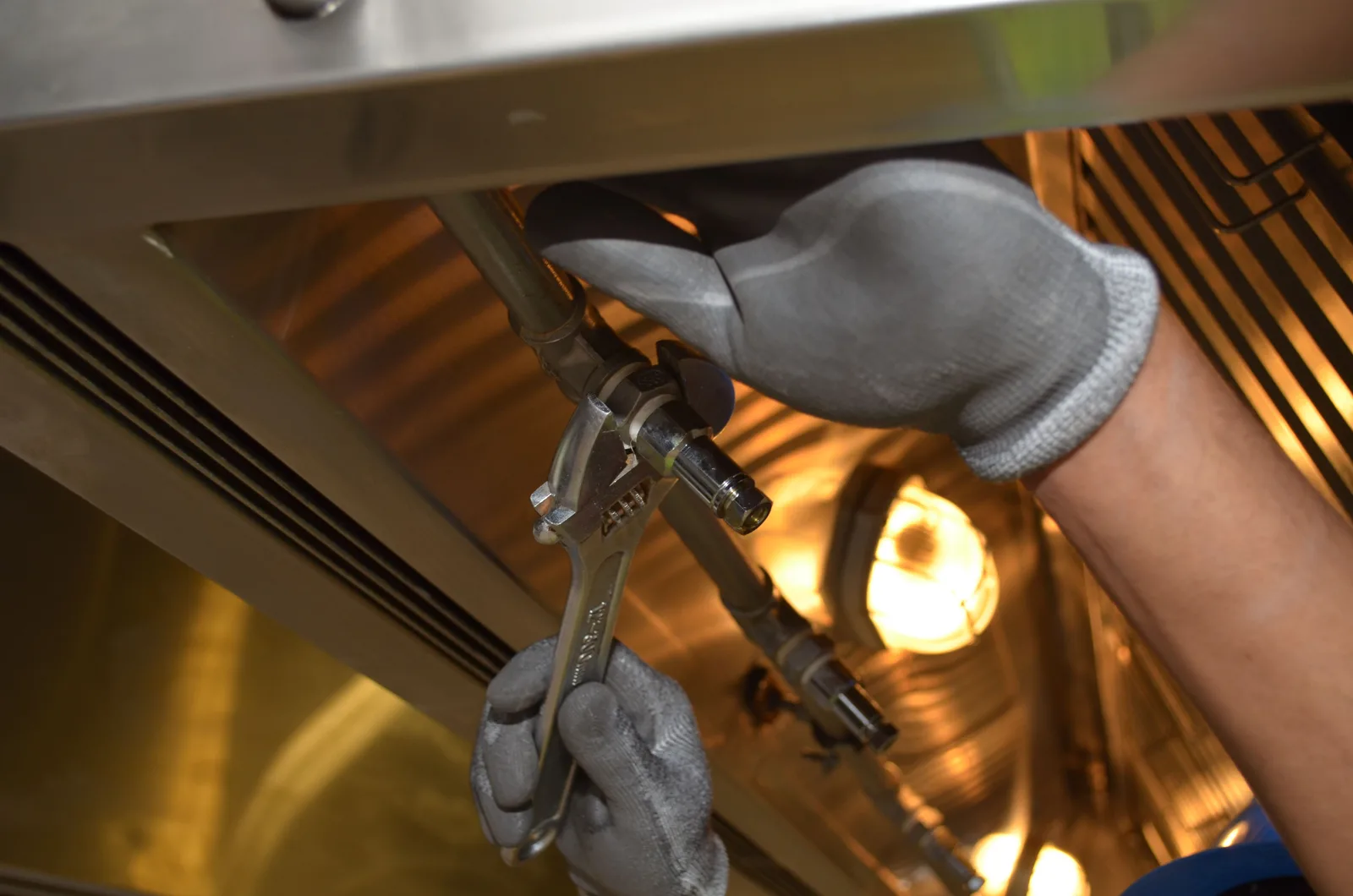 Gloved hands tightening a fitting on pipework with a wrench