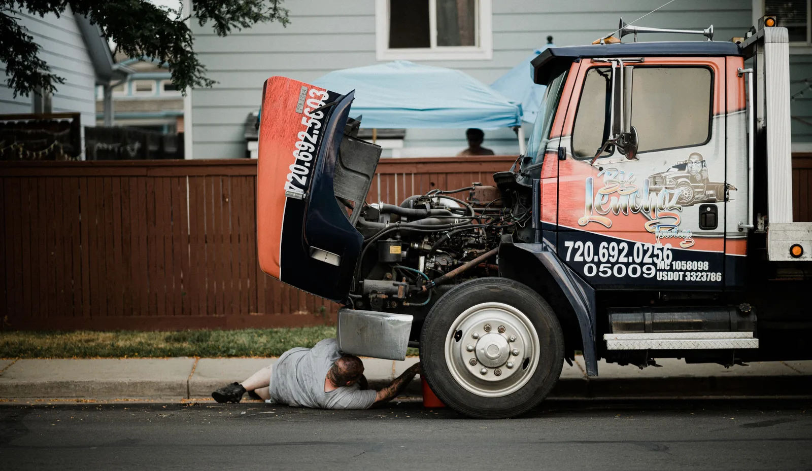 Mechanic lying under a box truck parked at the kerb, working on it.