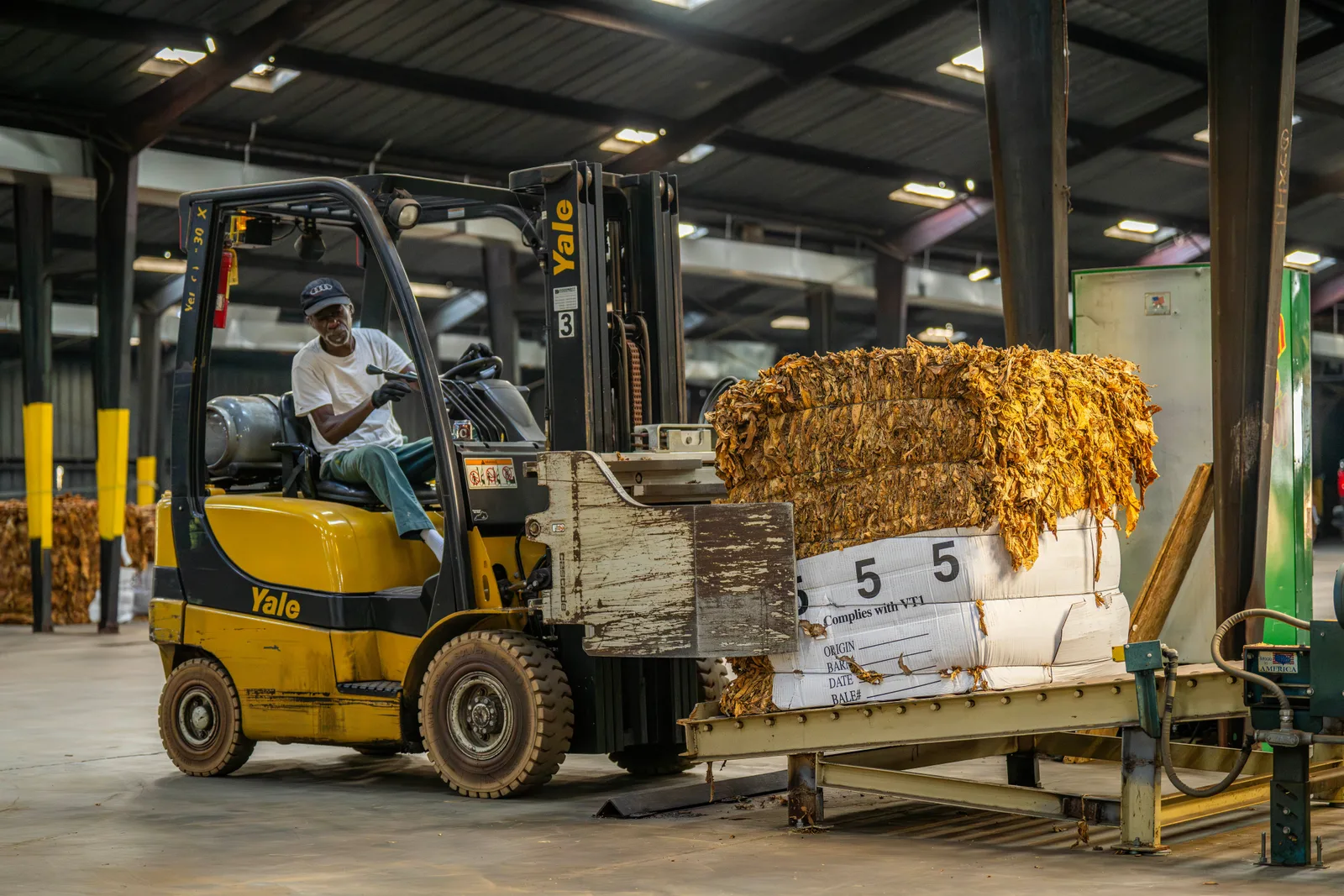 A forklift driver lifting a bale of packed material onto a press inside a warehouse