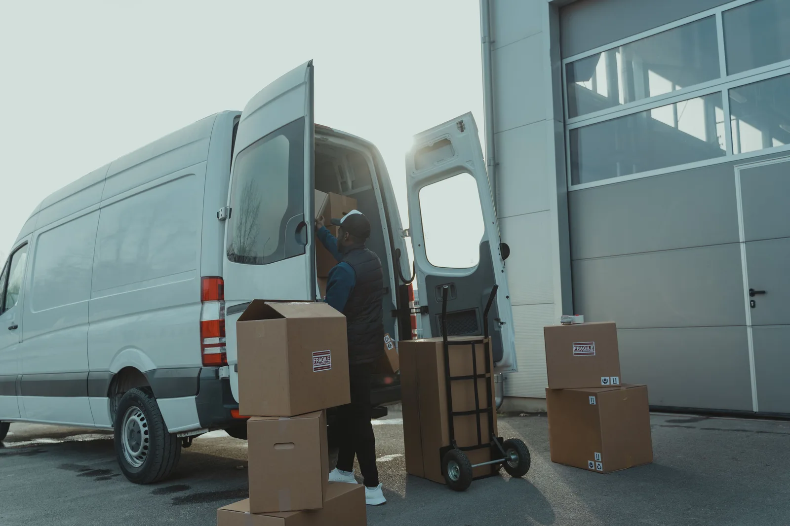 Courier loading cardboard cartons into the back of a delivery van outside a warehouse
