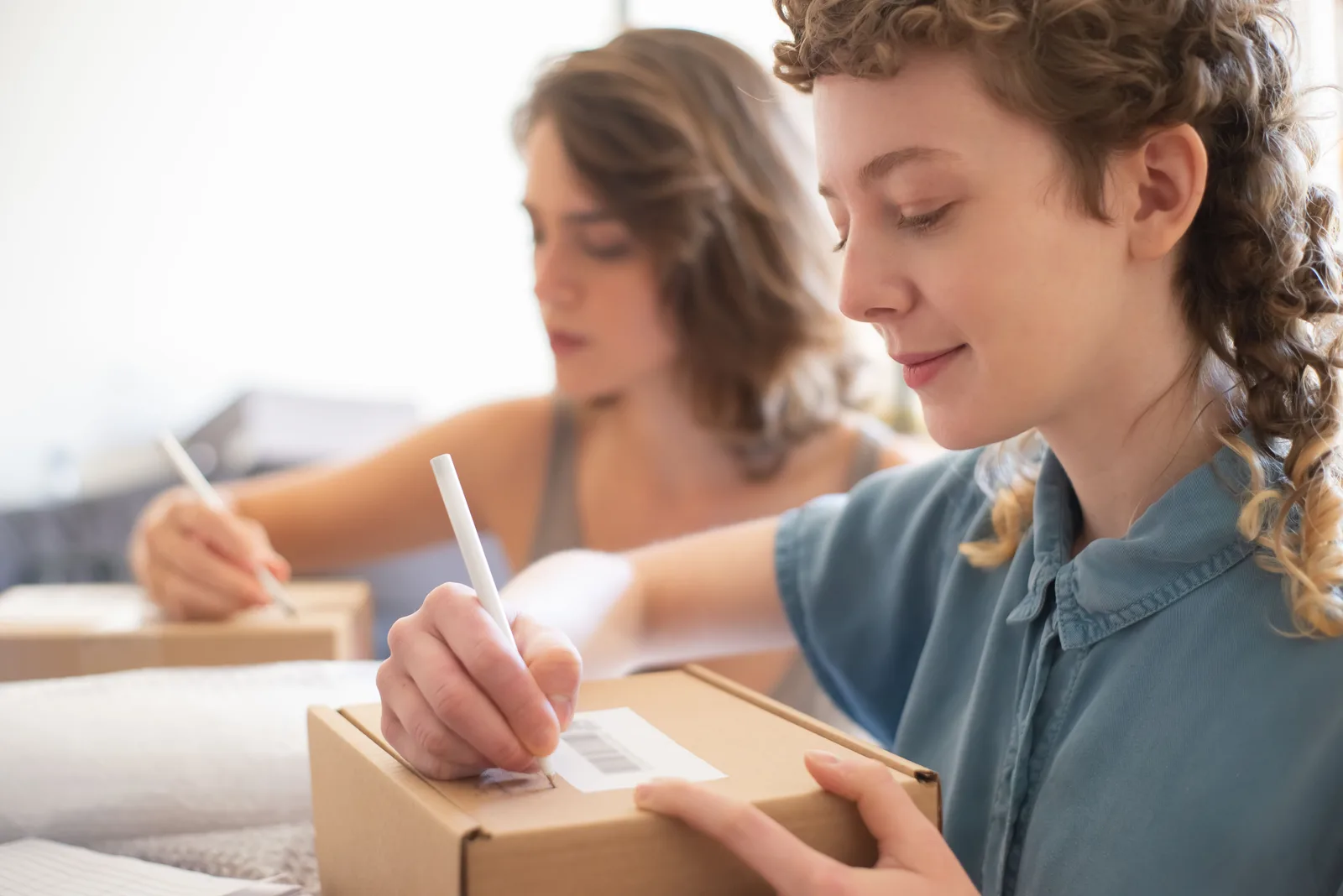 Two people writing details and applying barcode labels to shipping boxes