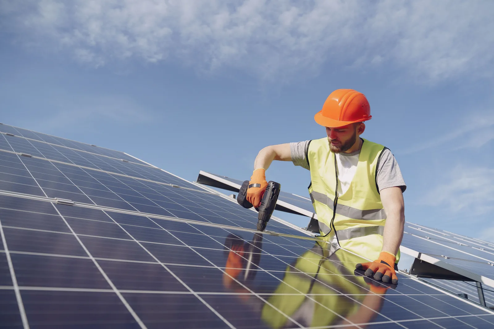 Un técnico con casco y chaleco de alta visibilidad perforando el marco de un arreglo solar en un techo