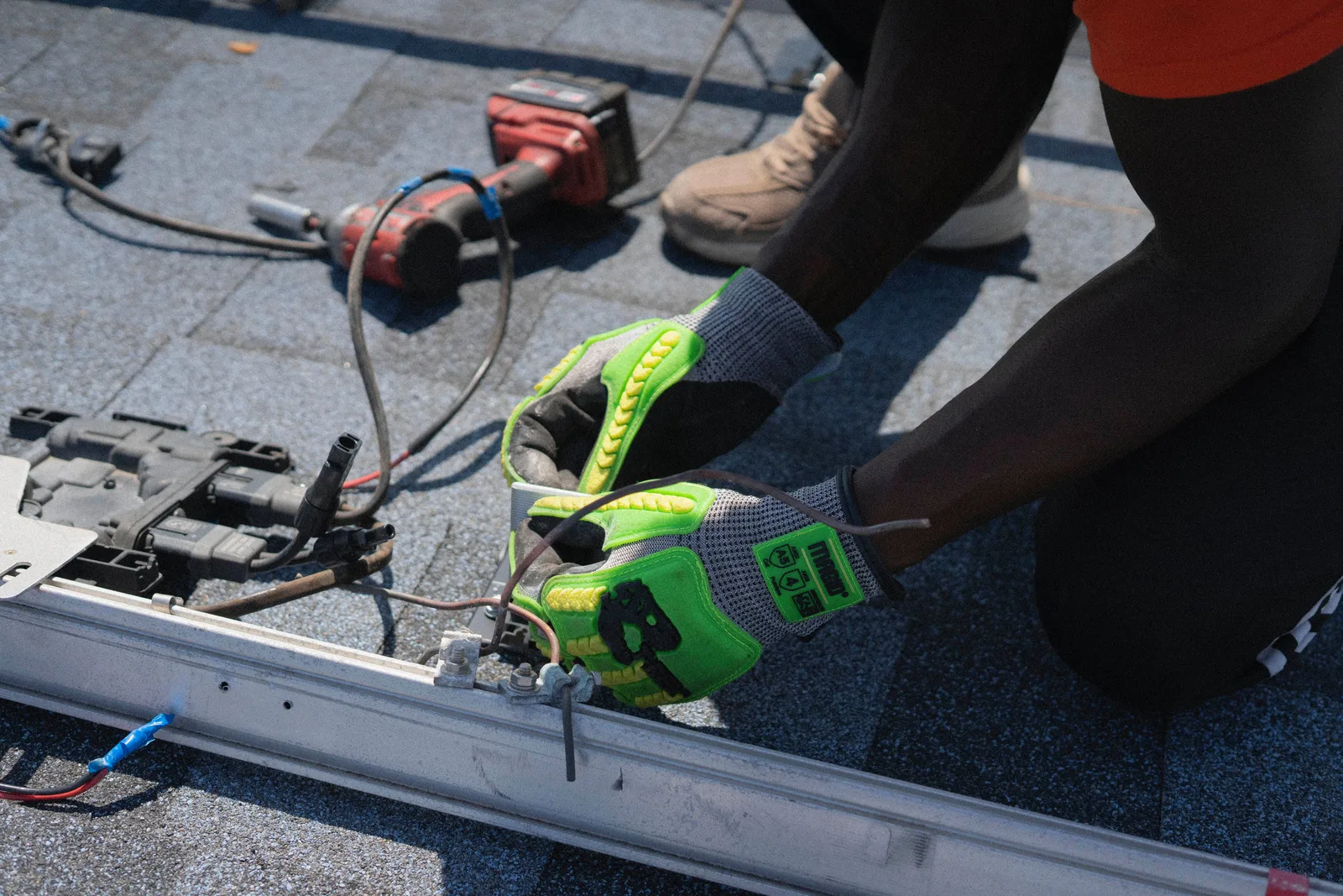 Gloved hands fastening mounting hardware to a solar panel rail on a roof
