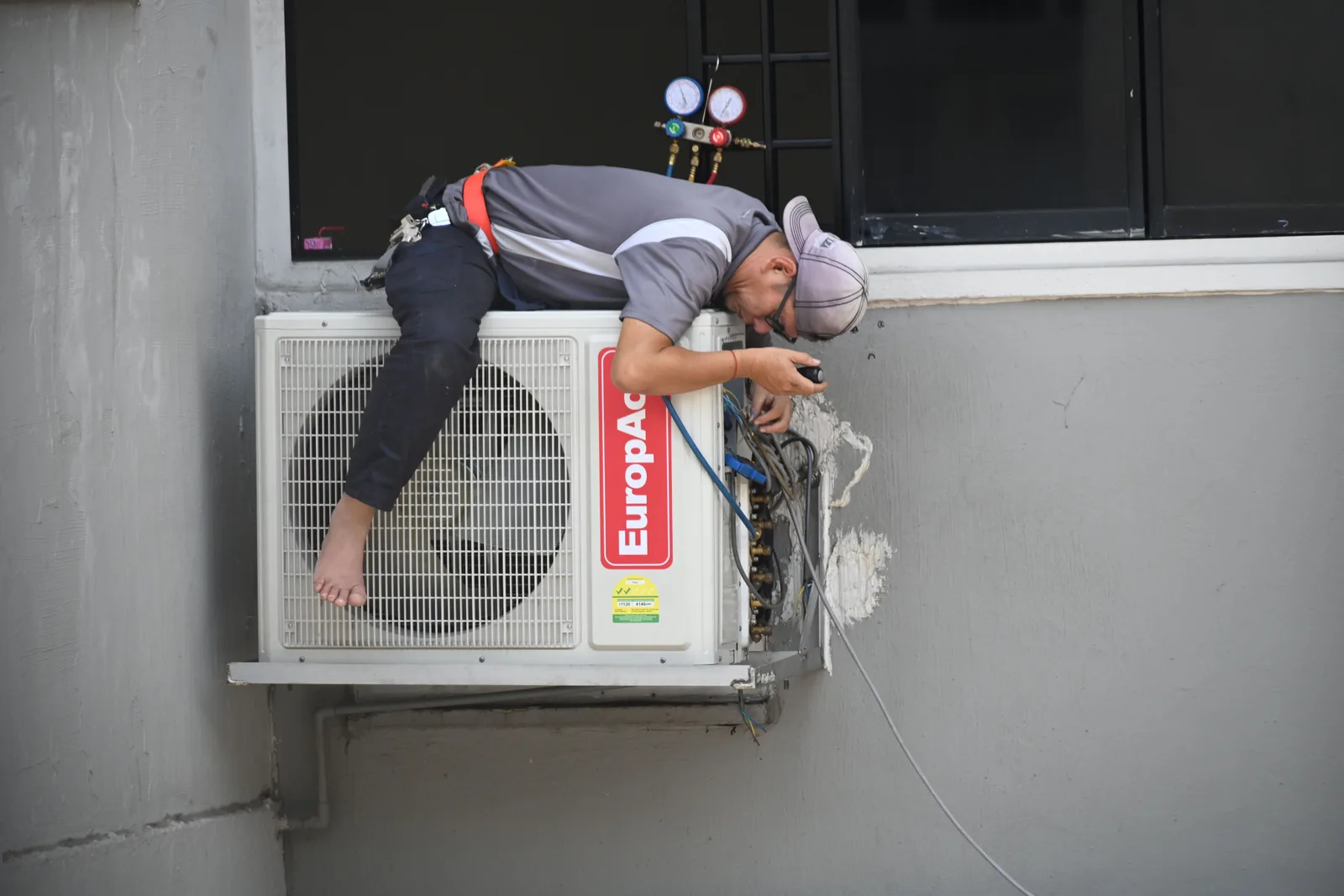 A technician working on an outdoor air conditioning condenser mounted on a building wall