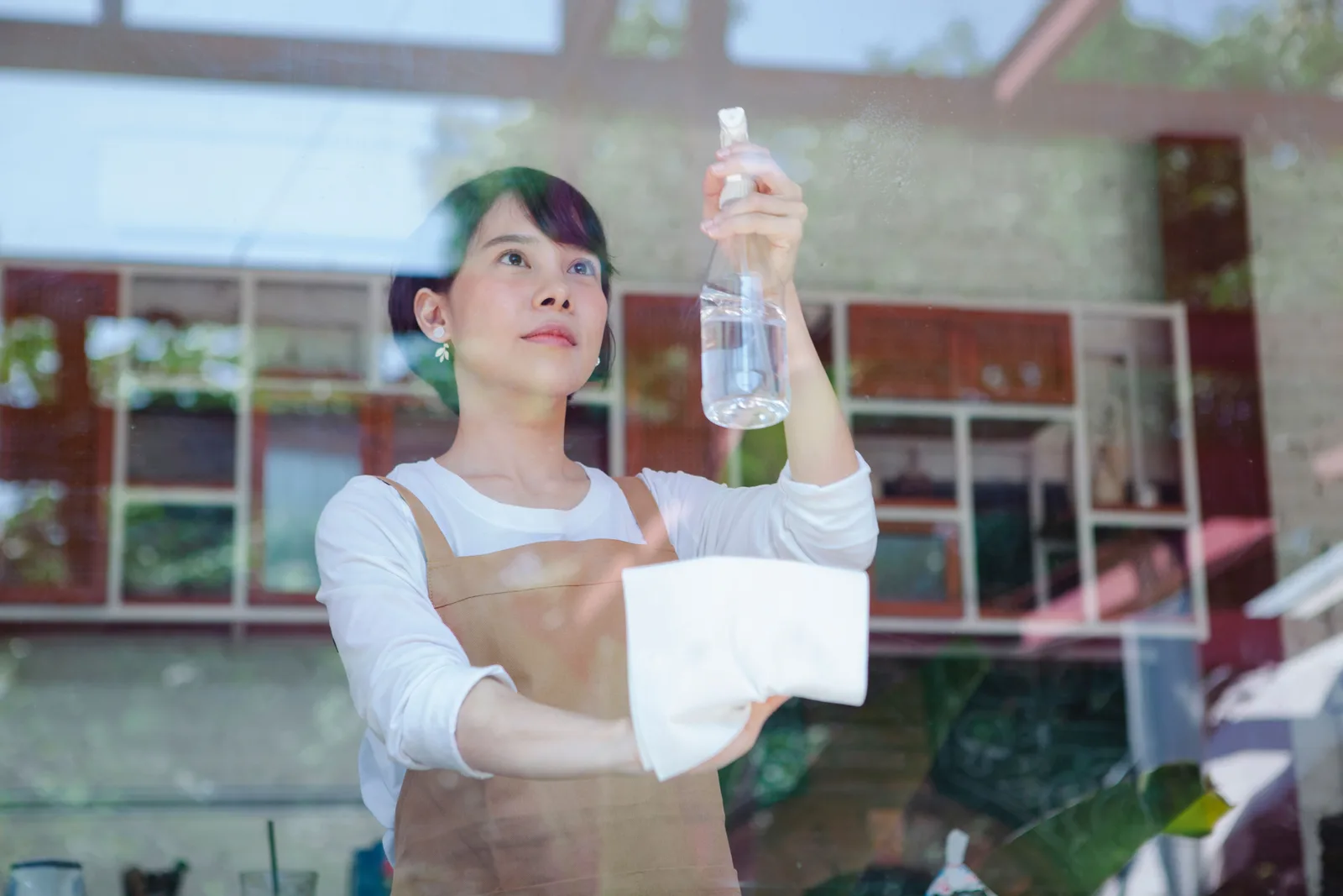 A cleaner in an apron spraying and wiping the inside of a restaurant window.