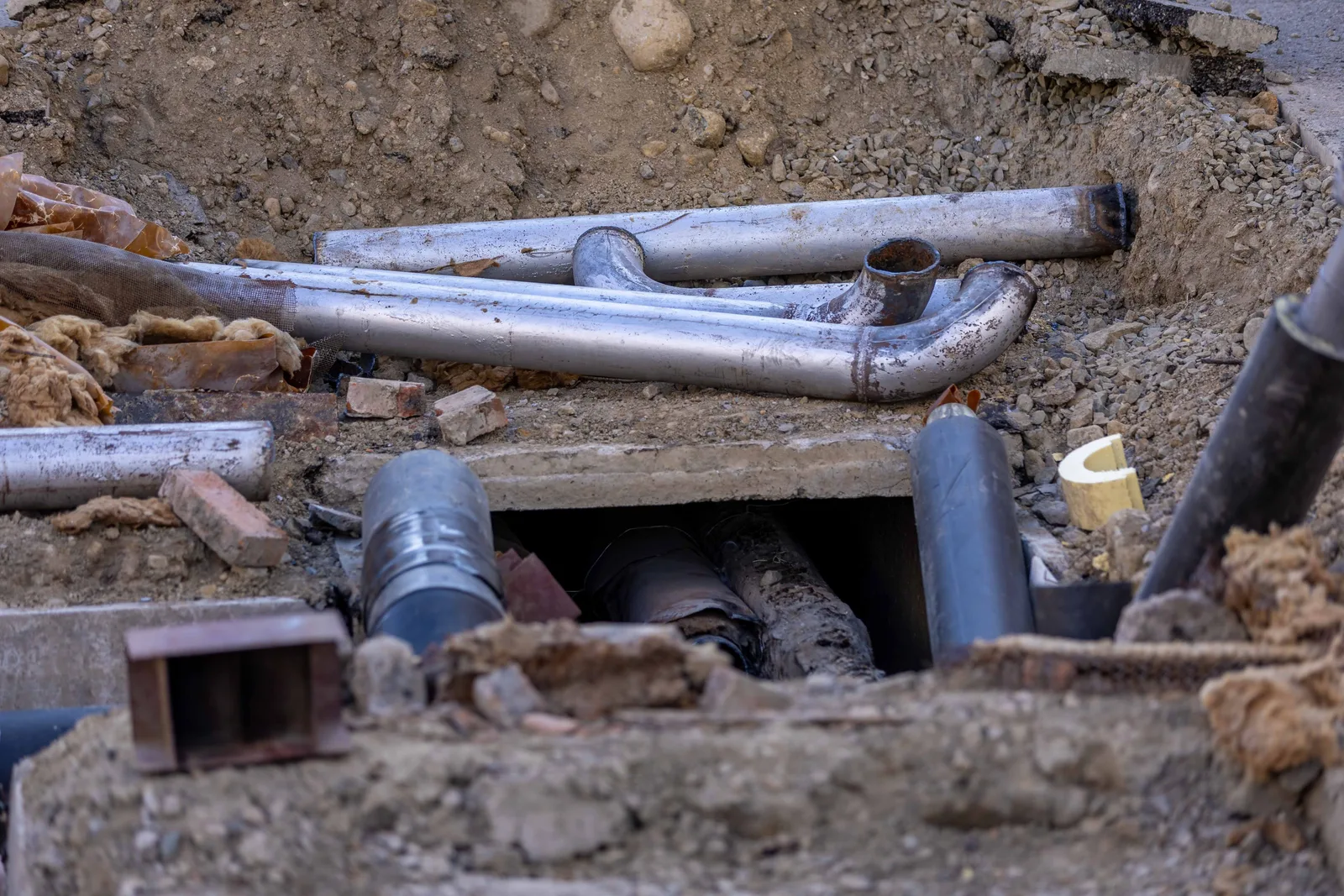 An excavated pit at a work site exposing old drain pipes and fittings below ground level