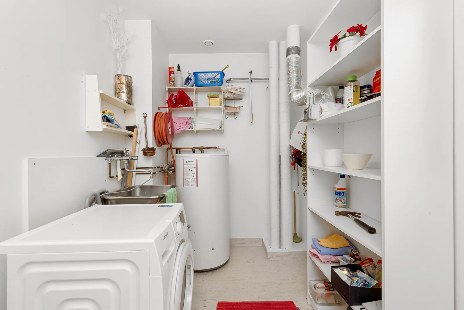 A home utility room with a white water heater standing beside a washer and shelving