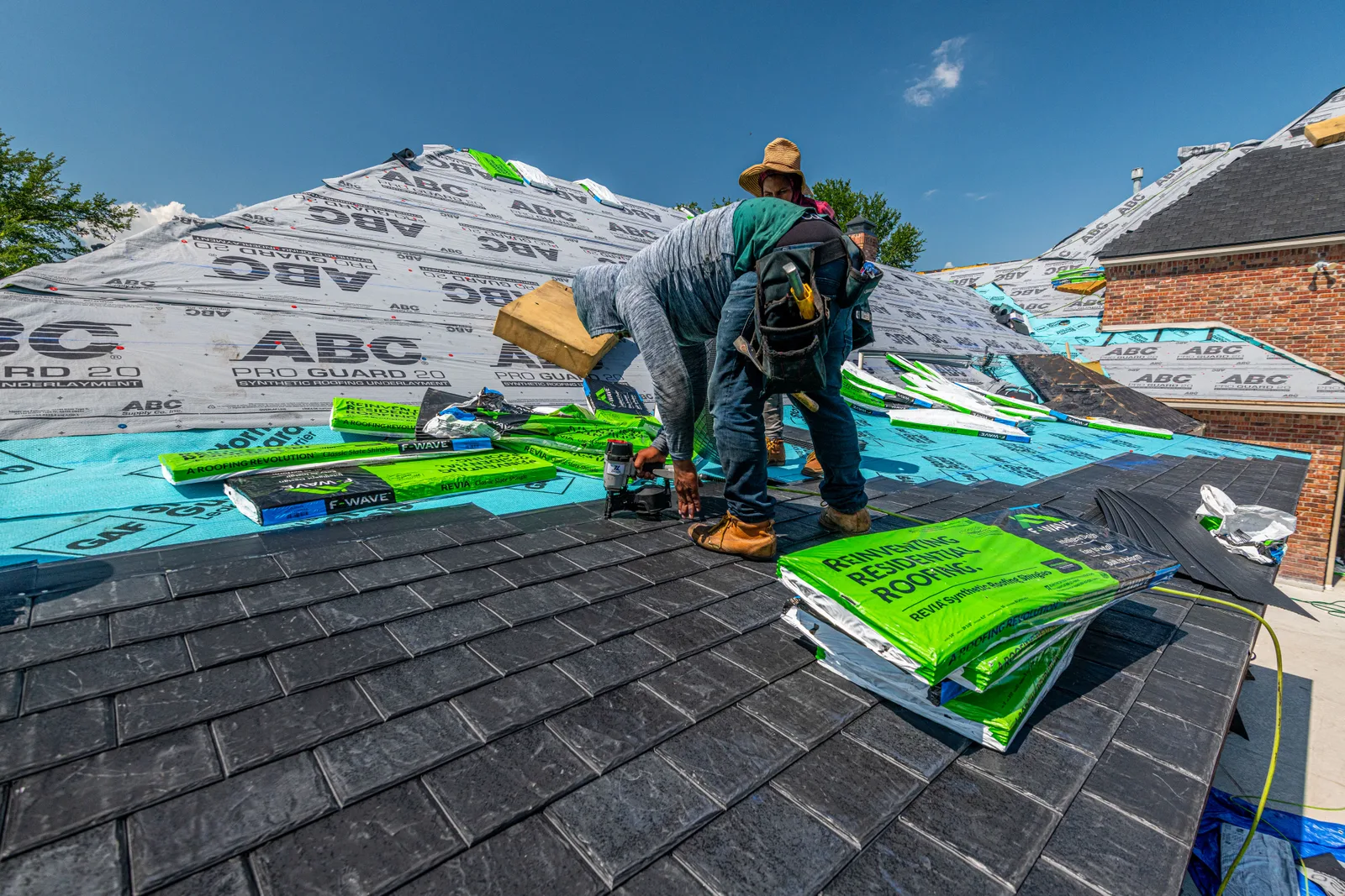Roofer on a steep roof with bundles of roofing material and rolls of underlayment staged around him